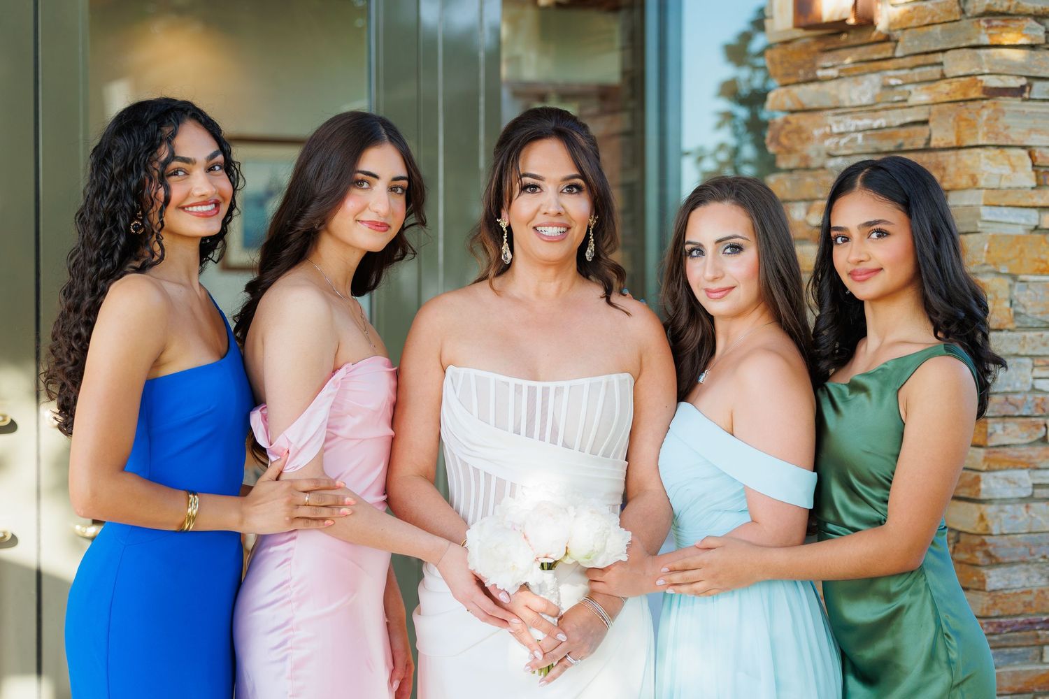 A group of people in formal attire pose together at an event with a stone wall backdrop.