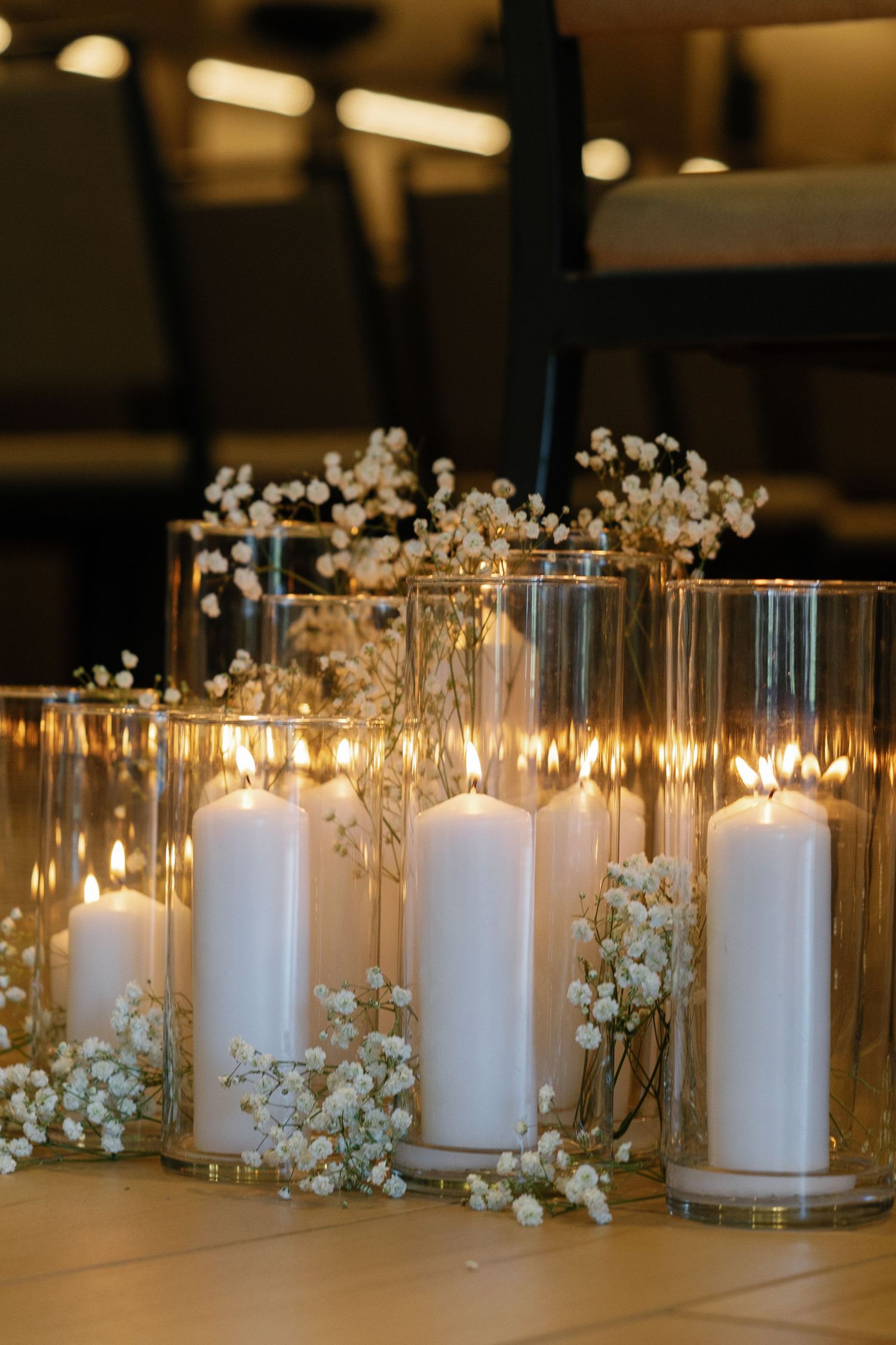 White pillar candles in glass cylinders decorated with delicate baby's breath flowers create an elegant wedding centerpiece display.