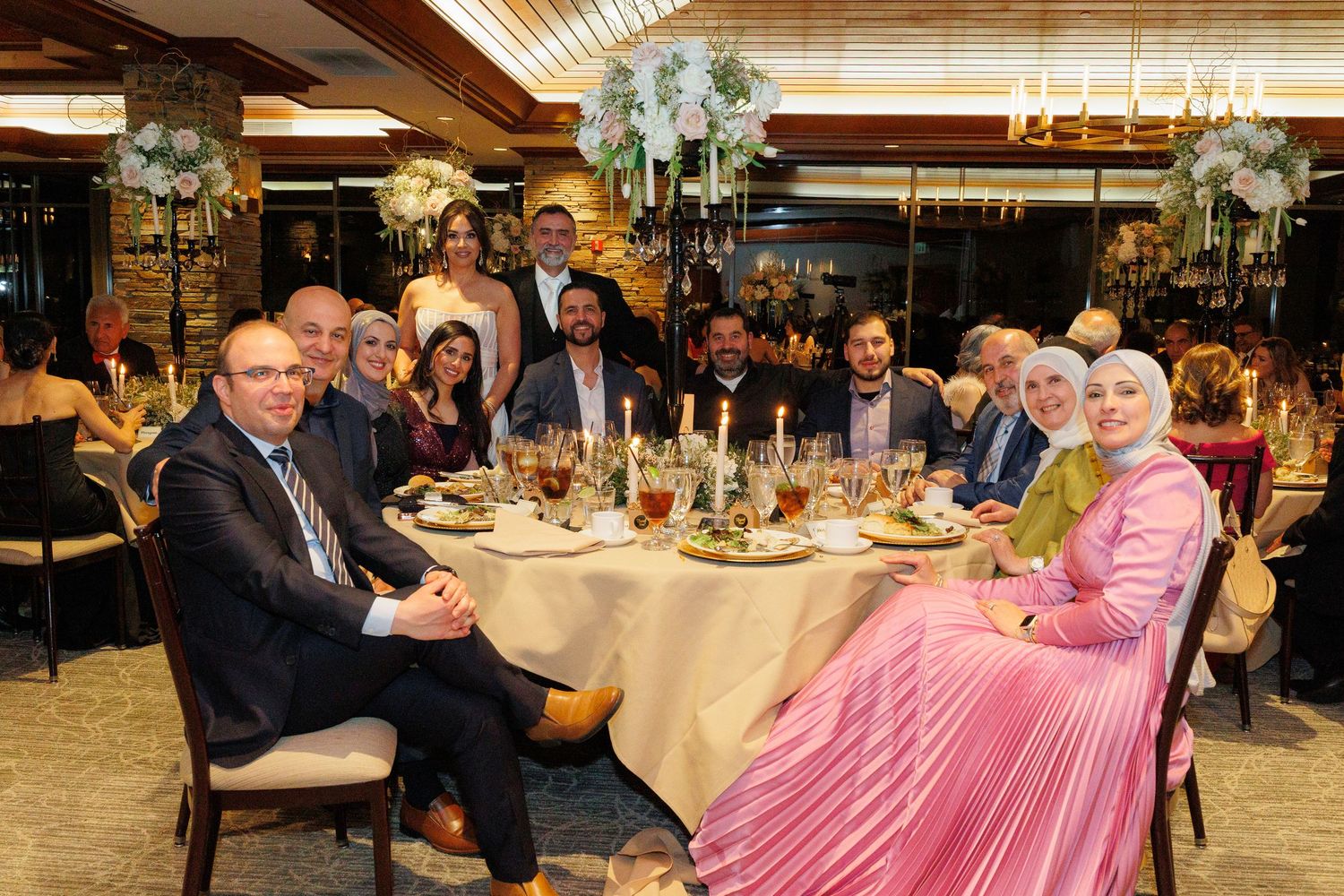 Wedding reception guests seated at elegantly decorated round tables in a banquet hall with floral centerpieces.