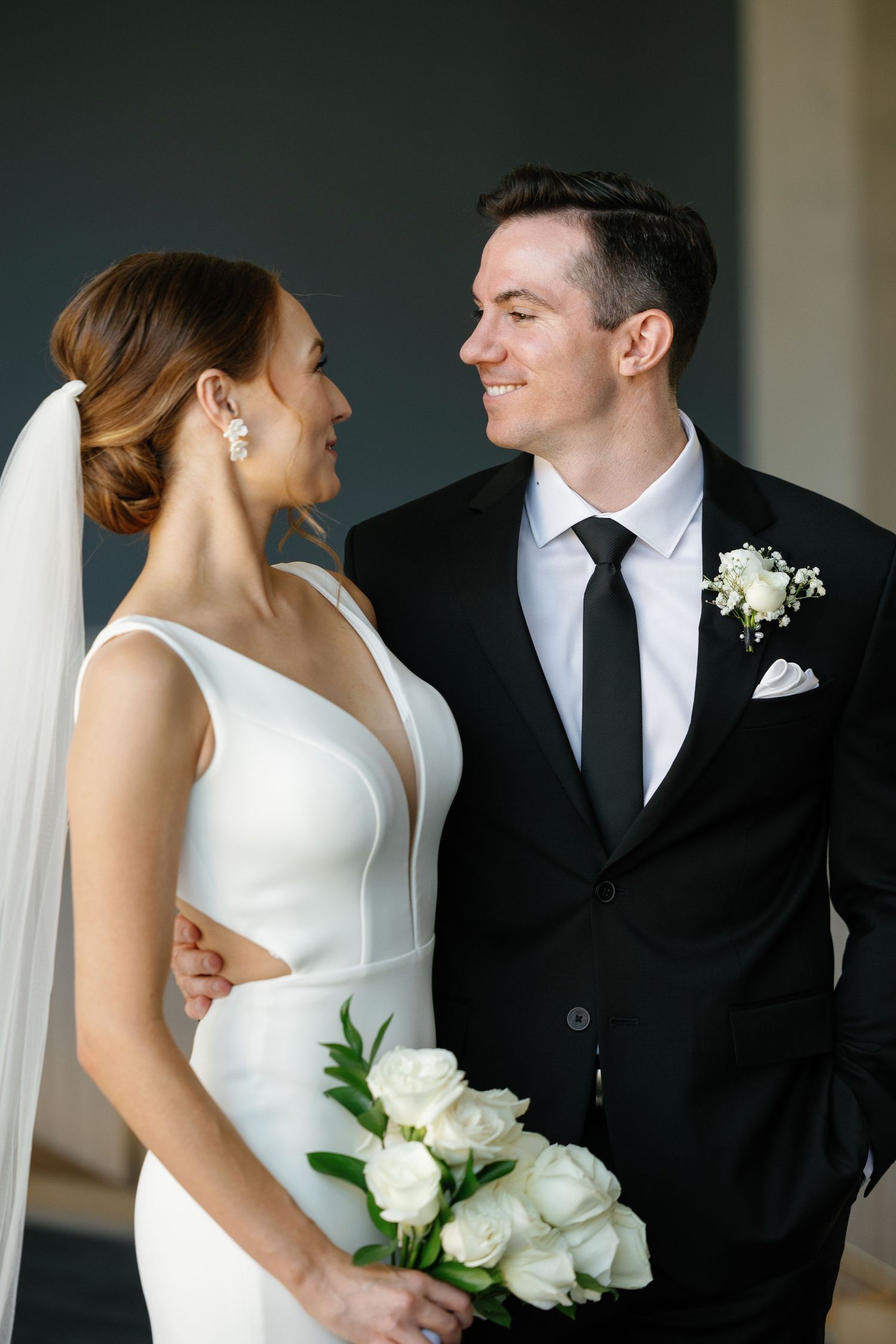 A romantic wedding couple in black and white formal attire share intimate moments while holding white roses.