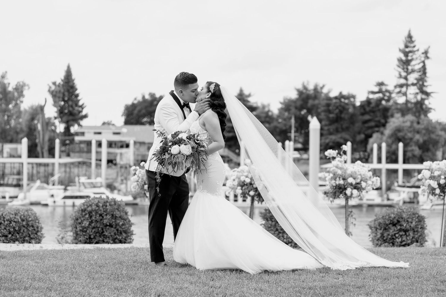 A bride and groom share a romantic moment in a garden setting with a flowing white veil in the breeze.