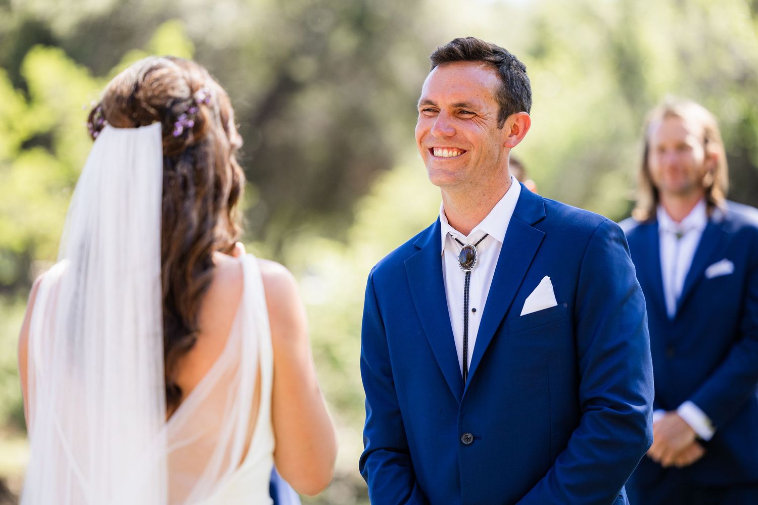 A couple shares a joyful moment during their outdoor wedding ceremony with guests looking on in the background.