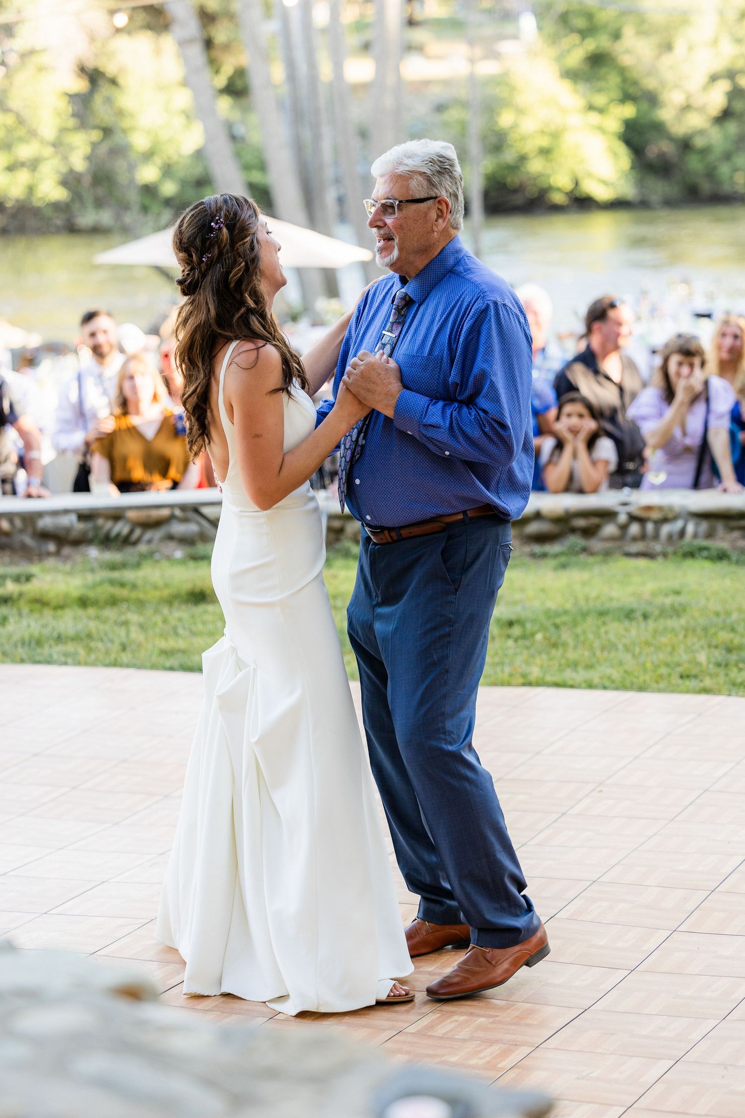 A couple dances together at an outdoor wedding reception on a stone patio during a summer afternoon.