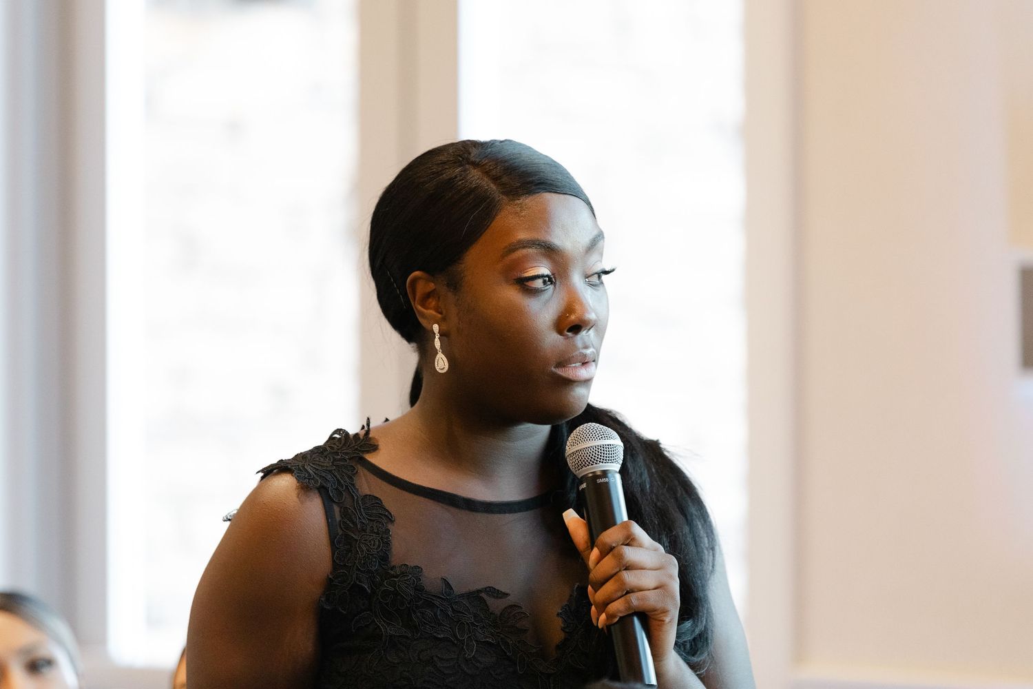 A speaker holds a microphone while wearing an elegant black sleeveless dress during a presentation.