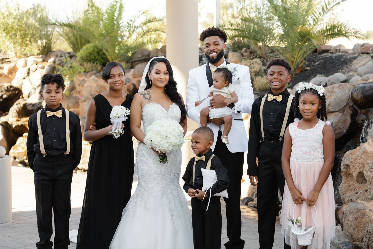 Wedding party members in formal black and white attire pose together outdoors during a celebration.