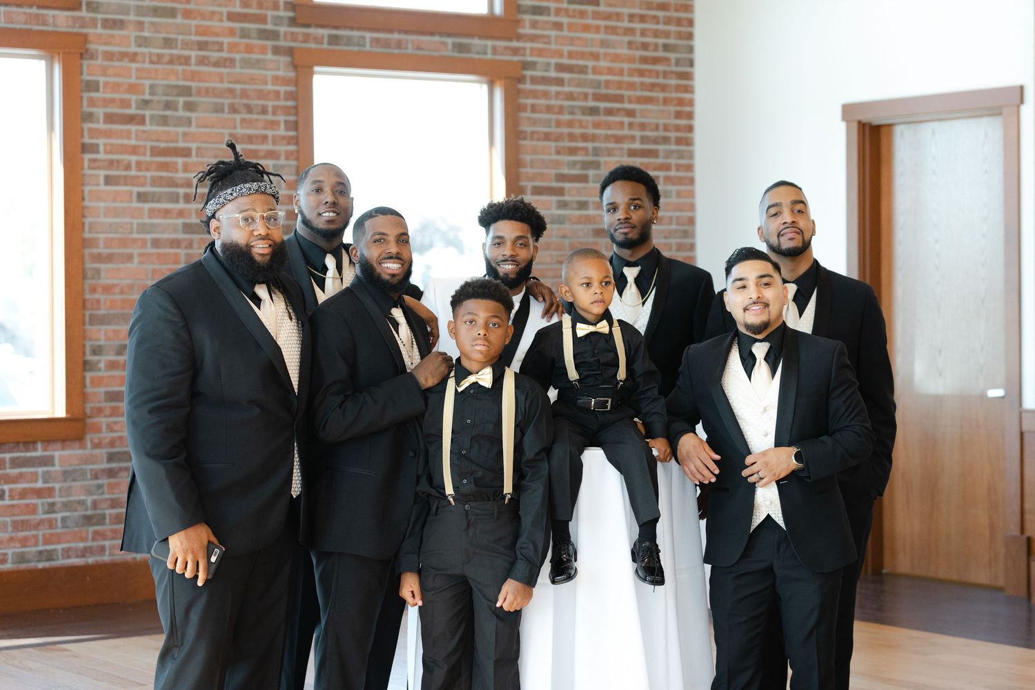 A group of people wearing black and white formal attire pose together in front of a brick wall.