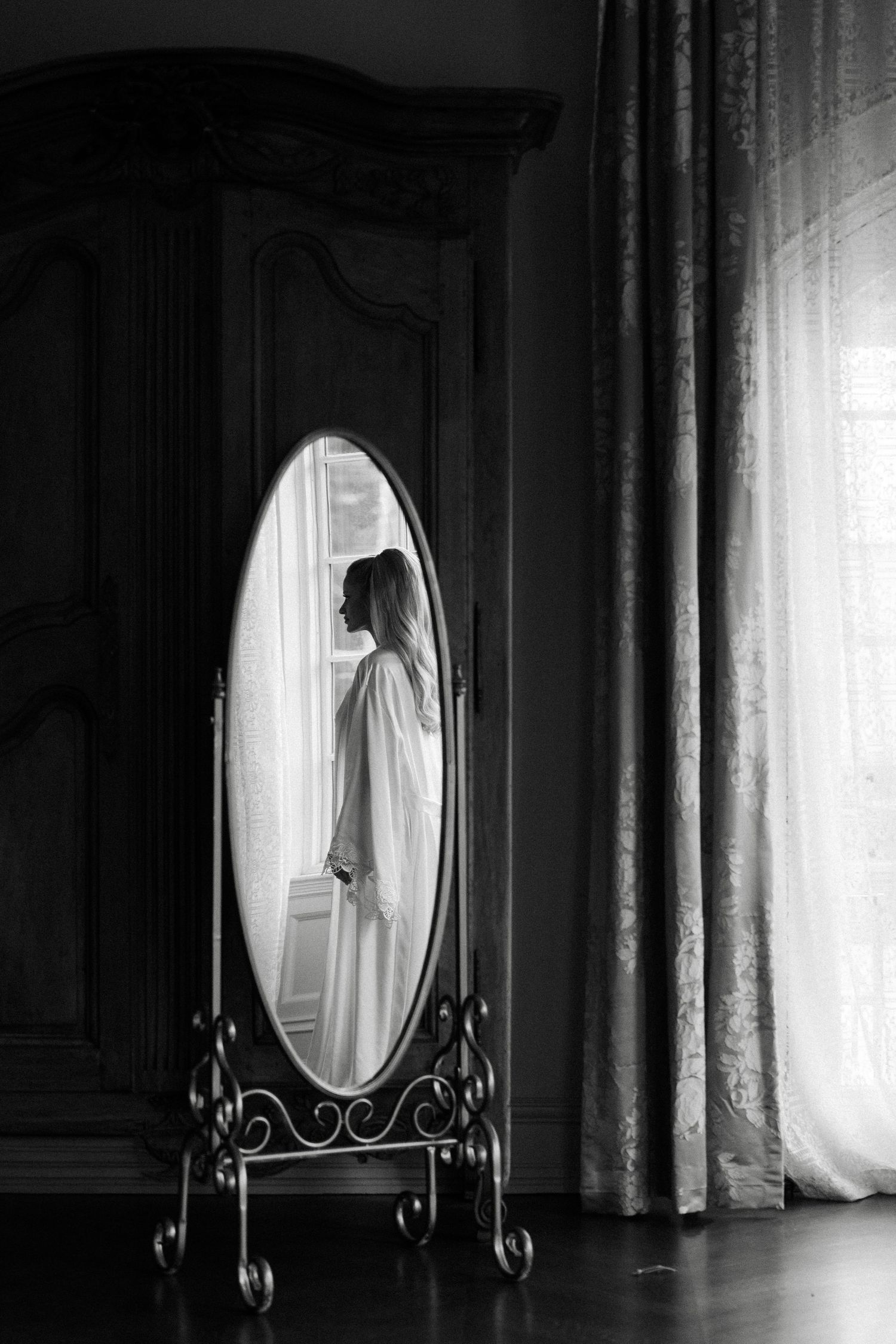 A silhouette reflected in an ornate standing mirror creates a dramatic black and white composition with window light.