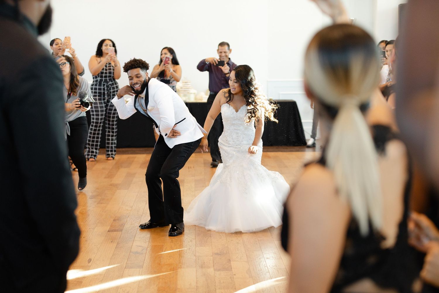 Wedding couple practices their first dance together in a dance studio with wooden floors and mirrored walls.