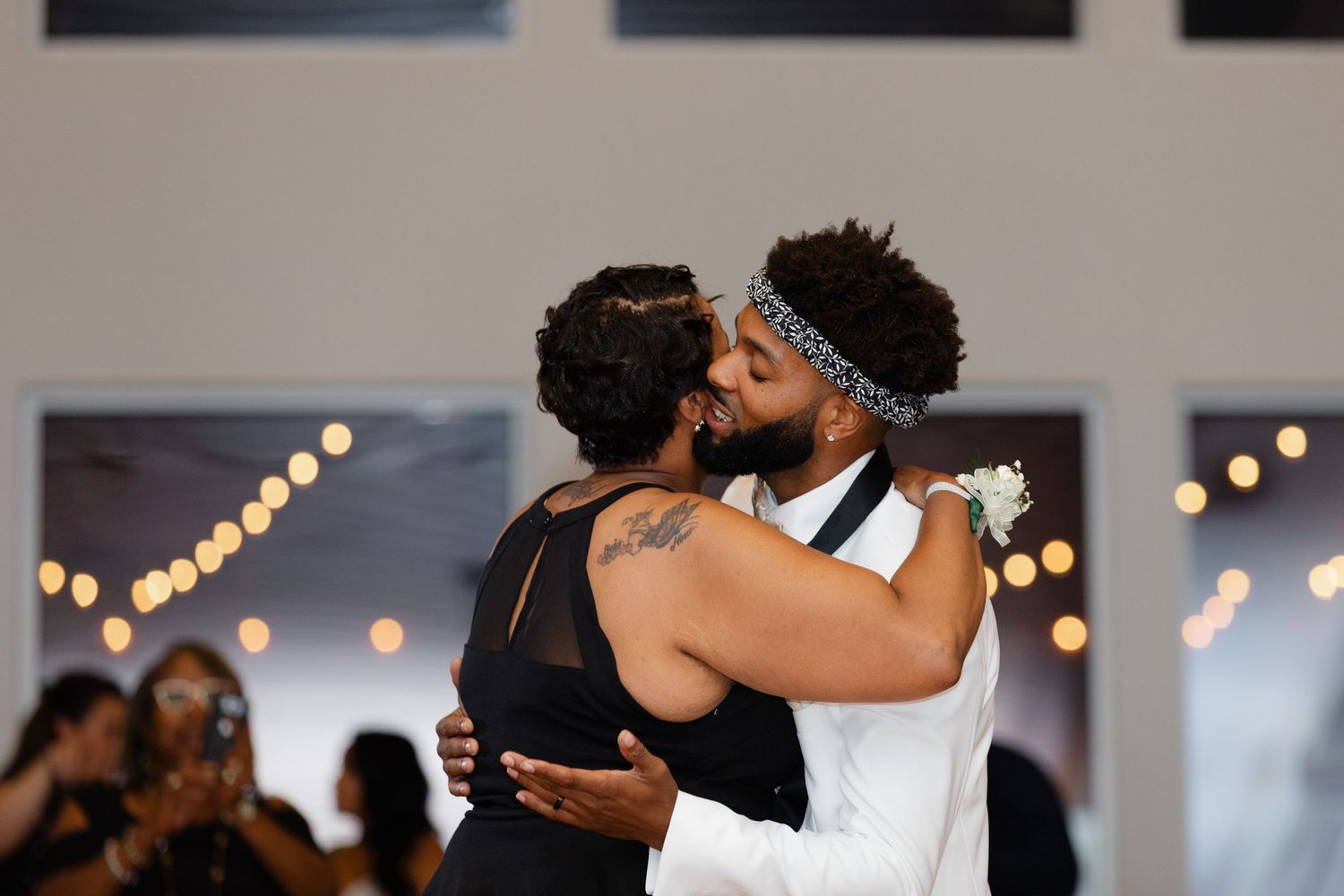 Two people share an intimate dance moment at an indoor reception with soft bokeh lights in the background.