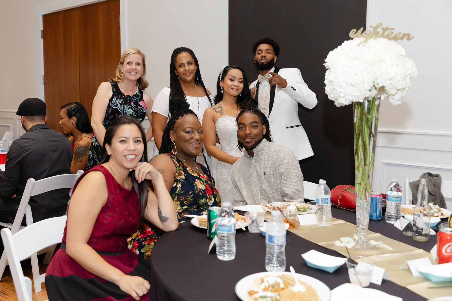 People gathered around tables at a professional event with white floral centerpieces and table settings.