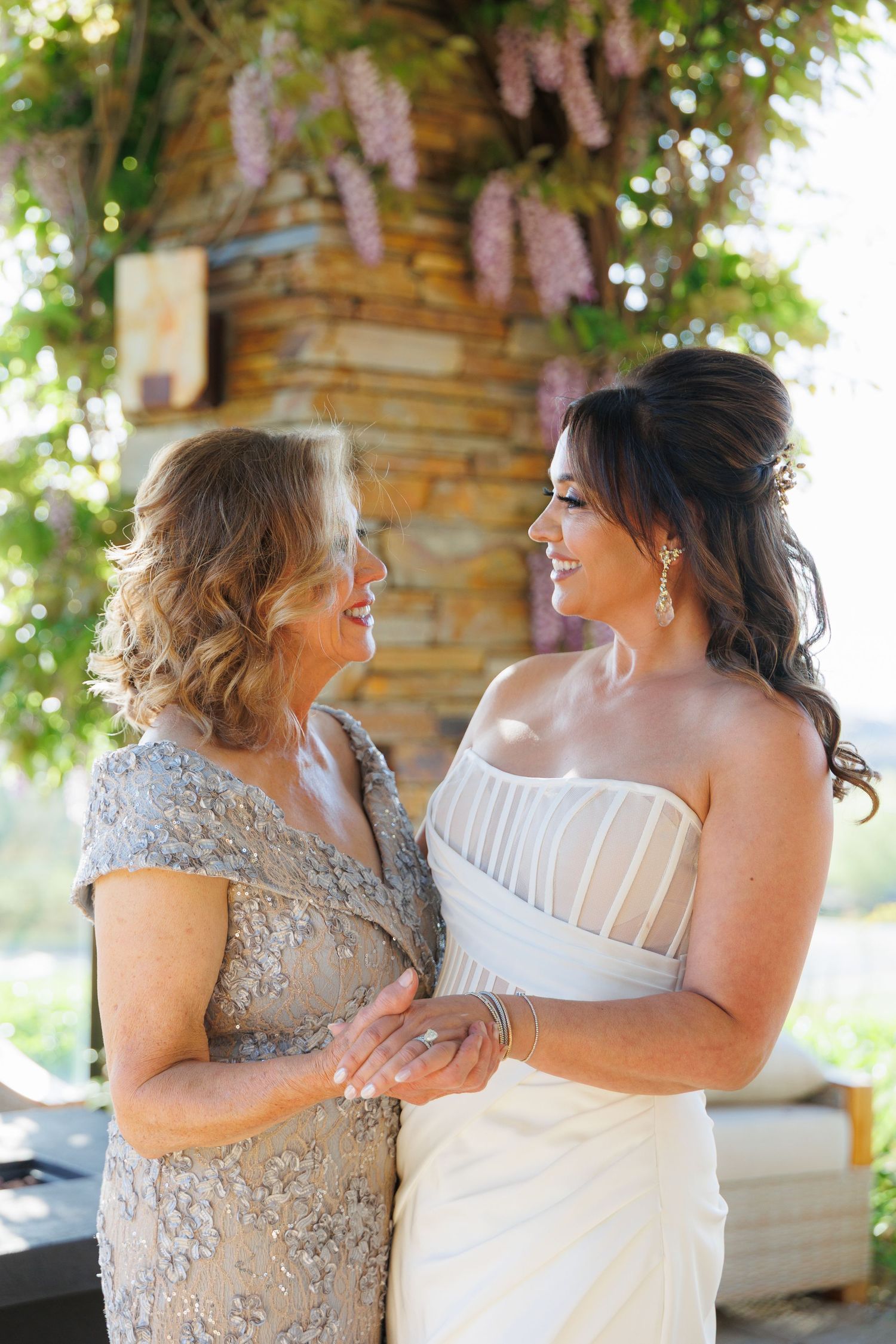 Two women in formal attire share emotional moments during what appears to be a wedding celebration on a patio.