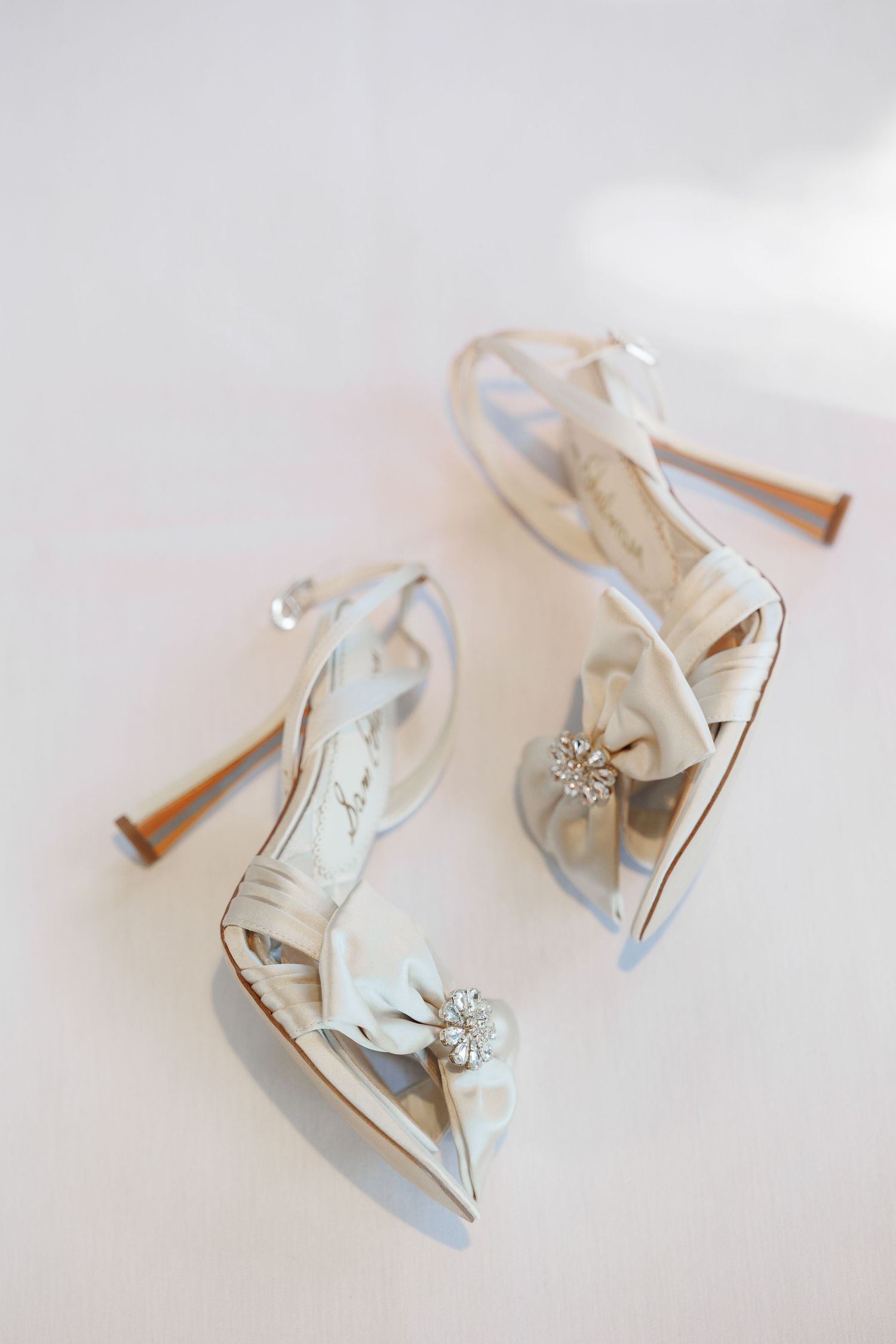 Elegant white satin bridal shoes with crystal embellishments and delicate straps photographed from different angles.