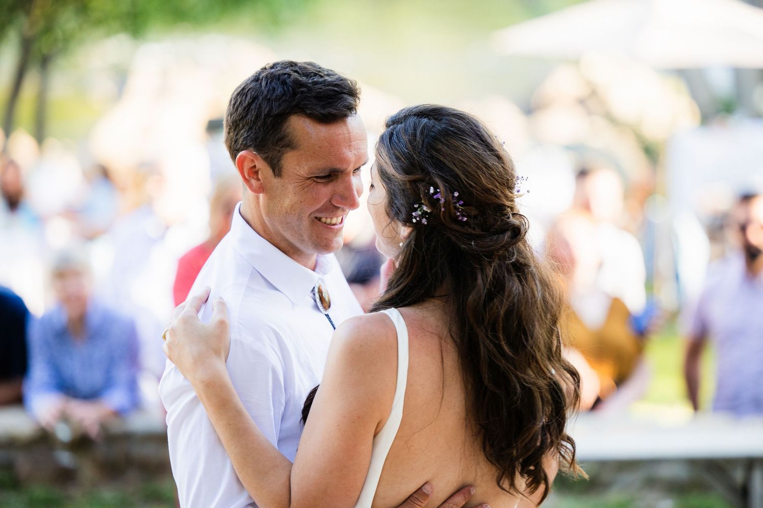 A couple dances together at an outdoor wedding reception as guests look on in the background.