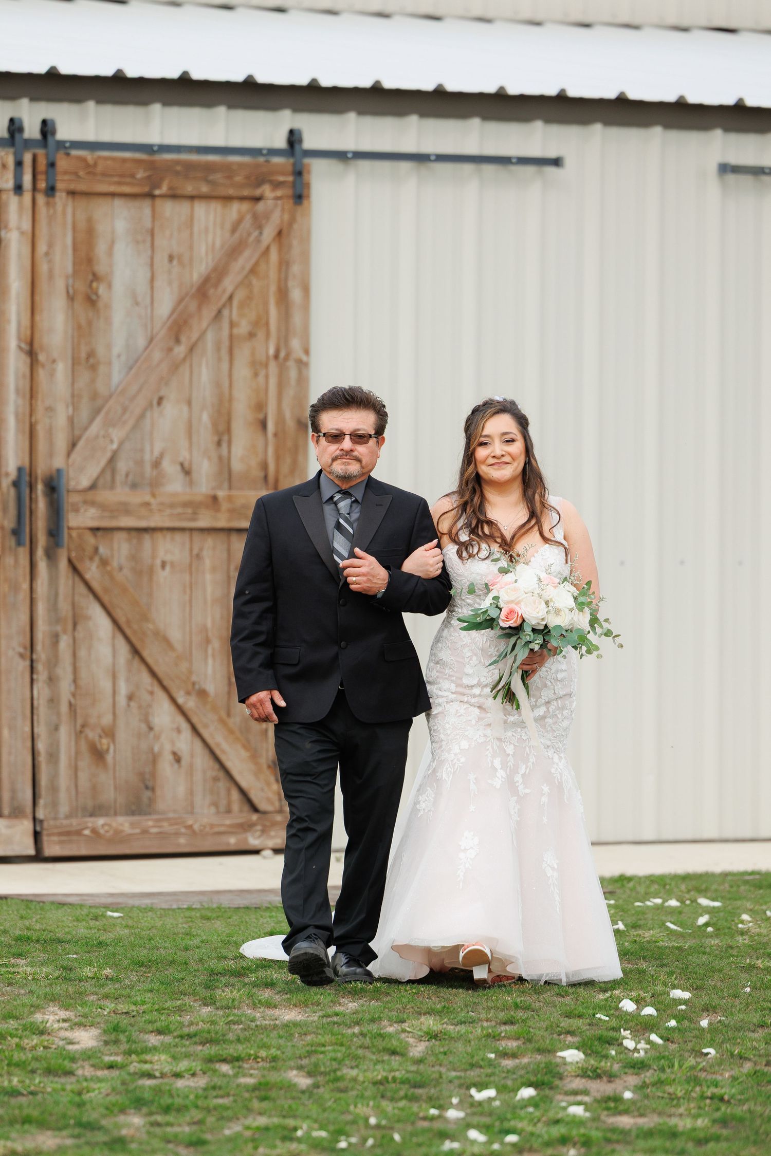 A wedding couple shares playful moments together in front of a rustic barn door setting.
