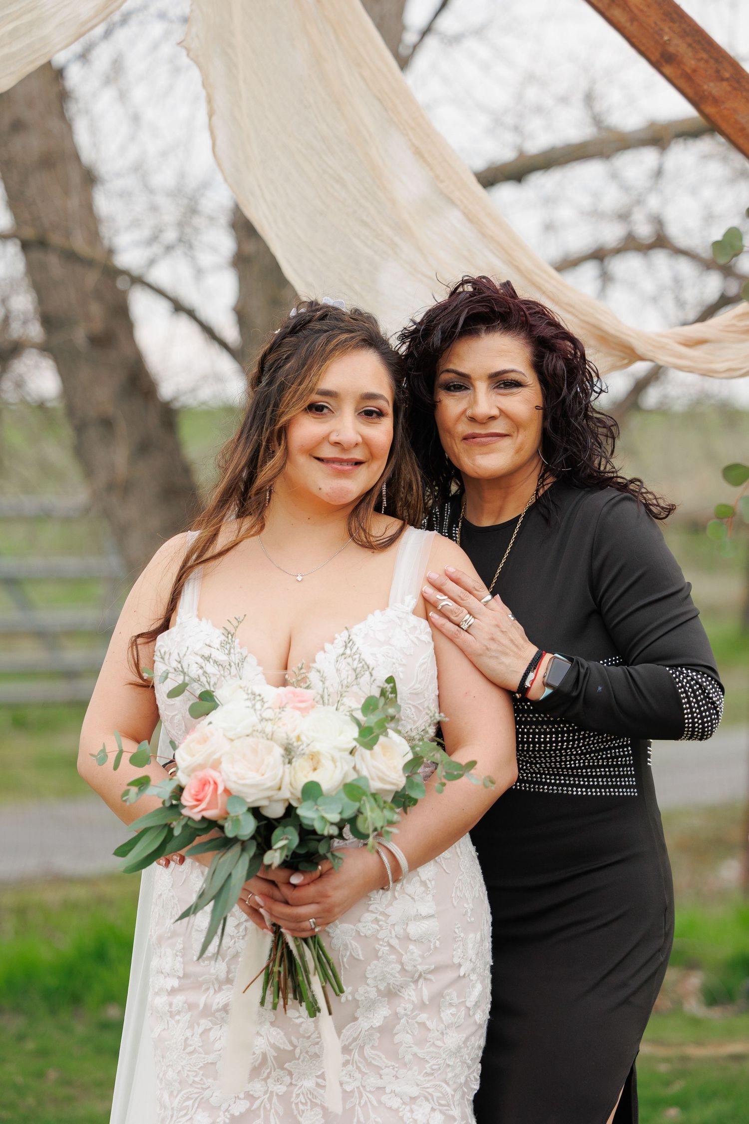 A tender moment captured outdoors with a bride in a white lace dress holding a pink and white floral bouquet.