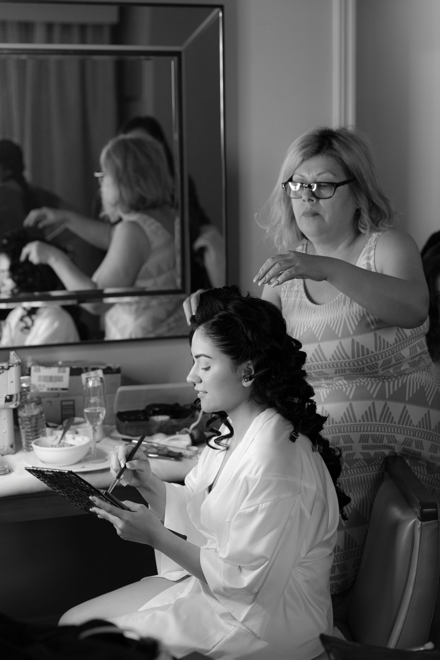 A sequence of black and white photos showing someone getting ready at a vanity mirror in a dressing room.