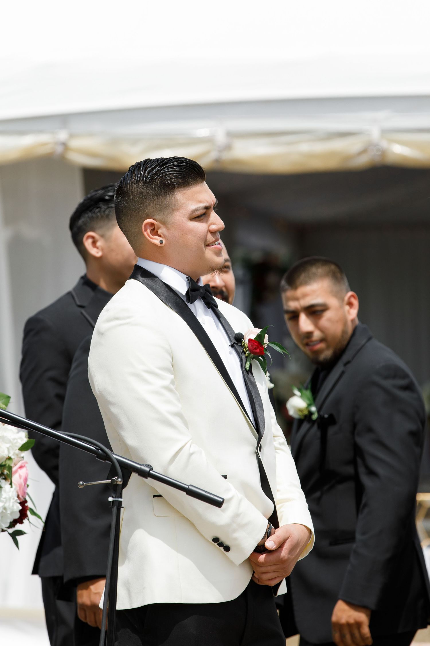 Groomsmen in white dinner jackets and black bow ties prepare for a formal wedding ceremony.