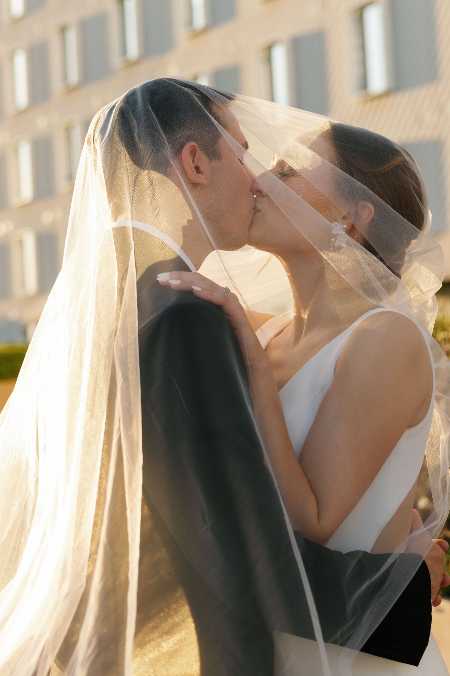 A tender wedding moment captured at sunset as newlyweds share a kiss beneath a delicate veil.
