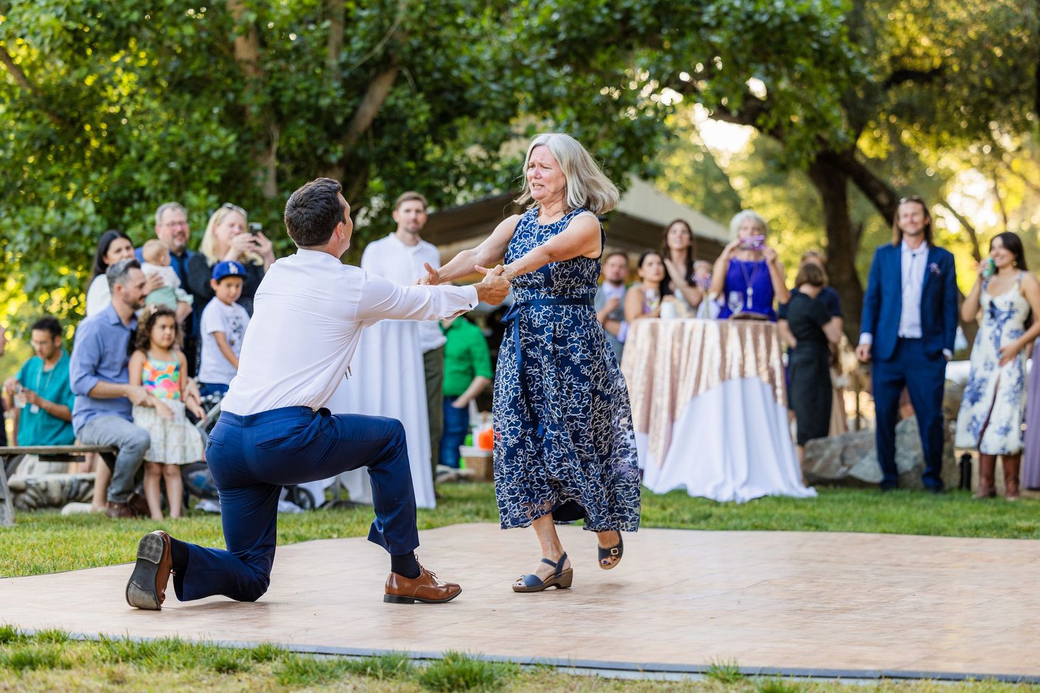 Wedding guests dance and celebrate outdoors at a garden reception venue during golden hour.