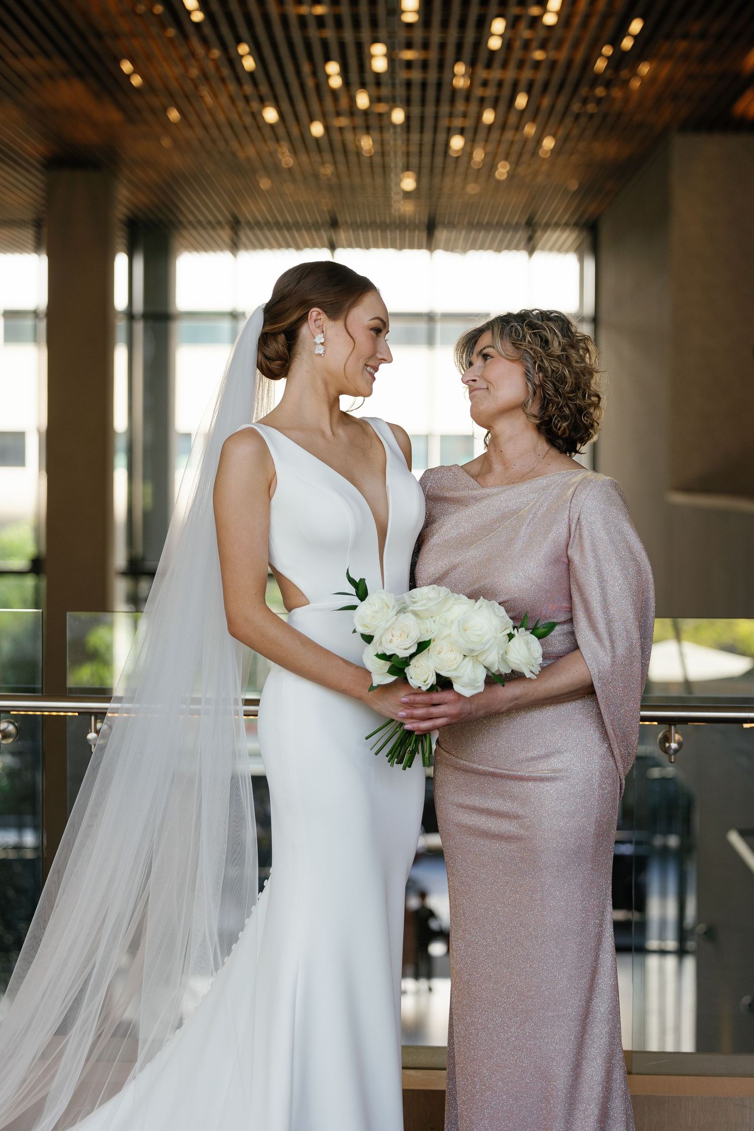 Two people share an intimate moment in formal attire with white flowers against an elegant indoor backdrop.