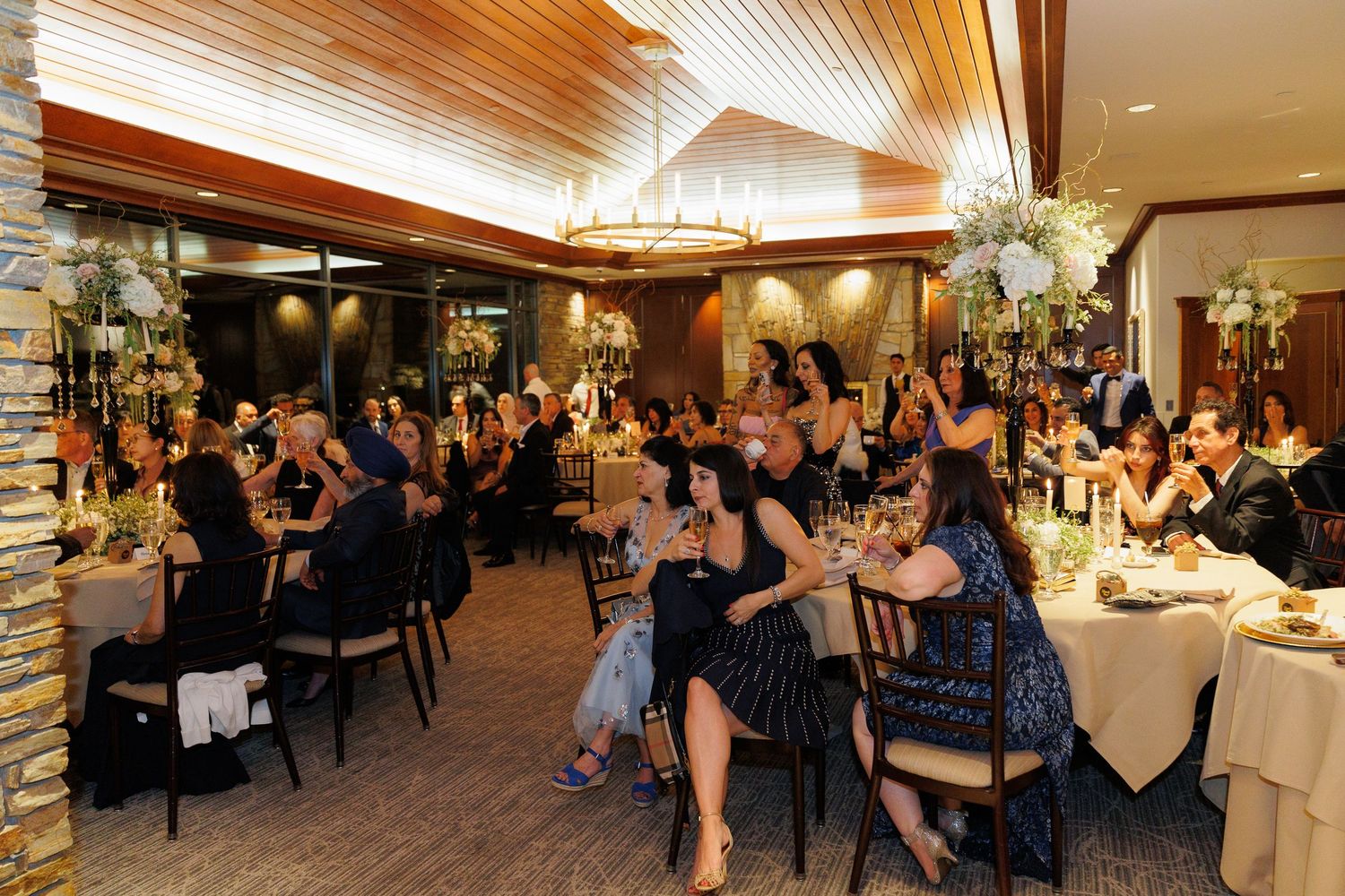 Elegant reception venue with wood-paneled ceiling and guests seated at tables during an evening celebration.