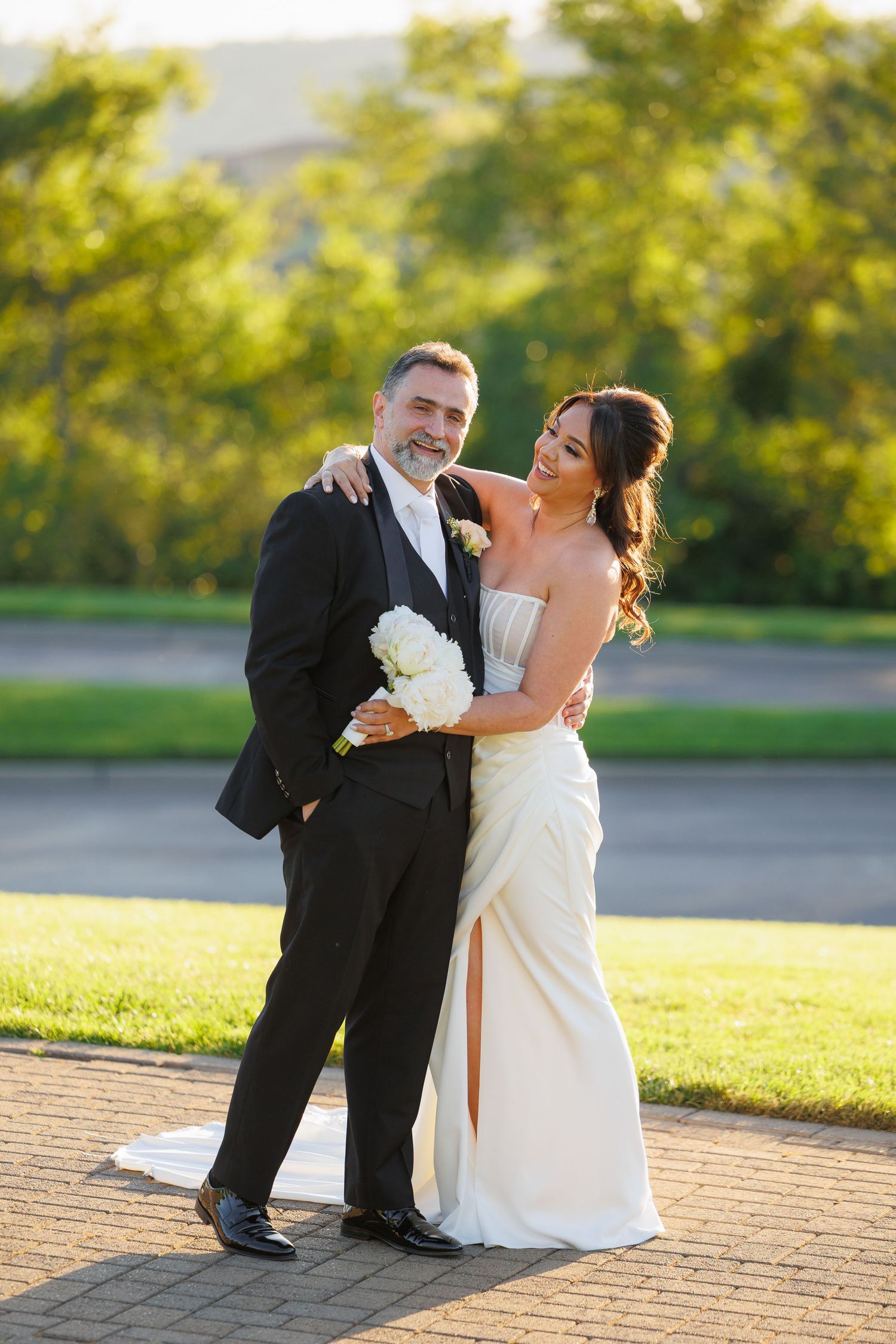 A couple in wedding attire shares a tender moment on a brick patio during golden hour.