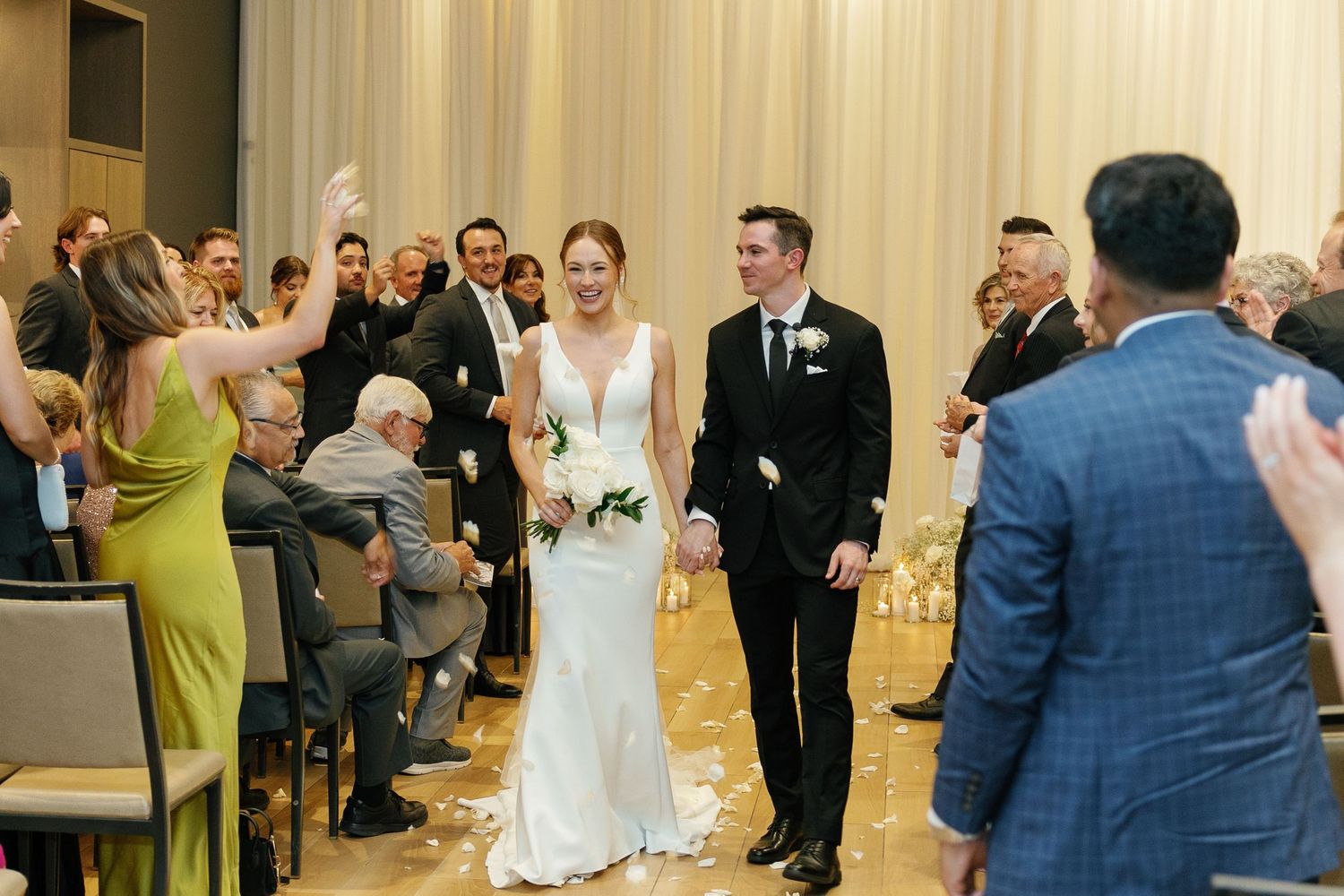 Wedding guests dance and celebrate during a lively reception in a bright indoor venue.