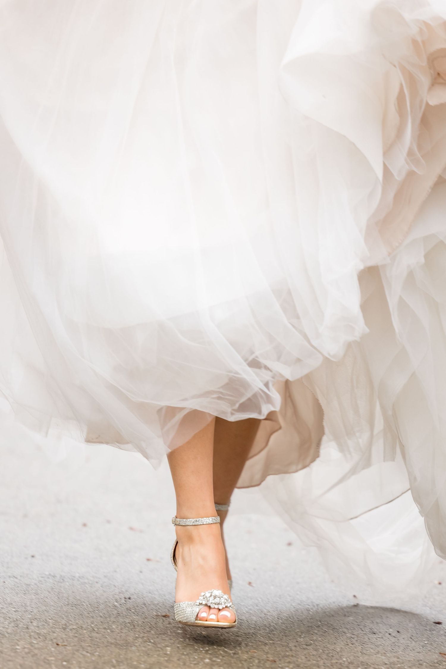 Flowing white wedding dress hem and sparkly bridal shoes captured in motion on light colored floor.