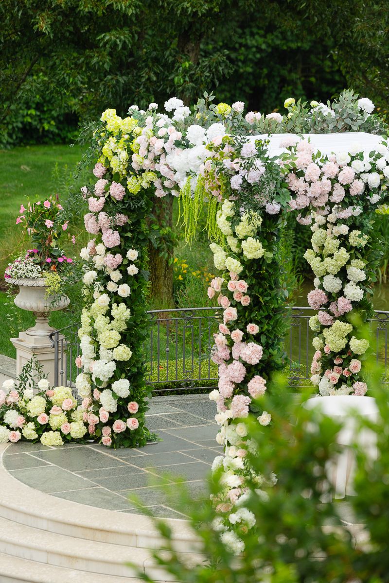Elegant floral arch with pink and white roses decorates an outdoor garden pathway.