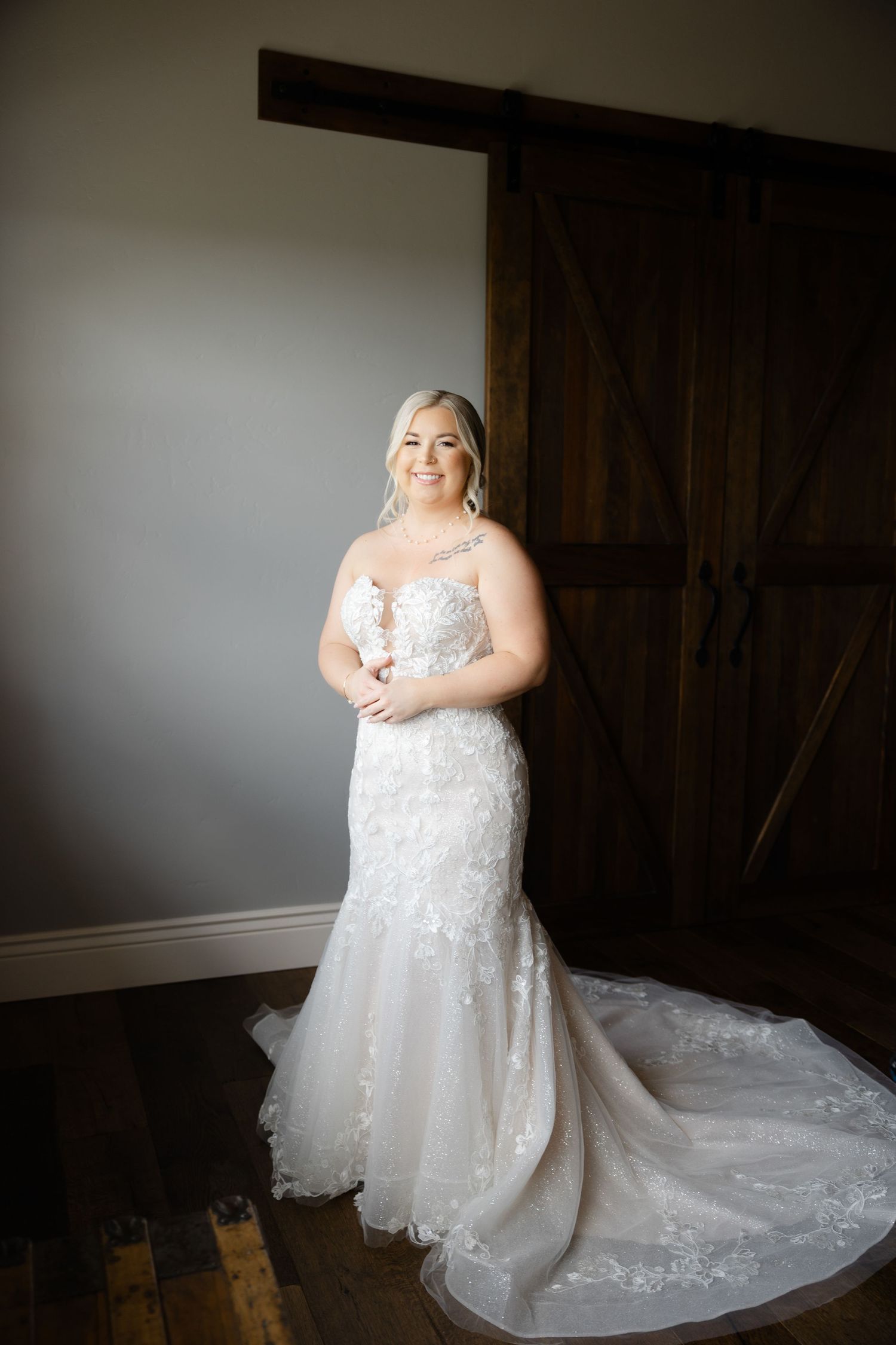 Bride in lace wedding gown poses against dark background showing full dress details.