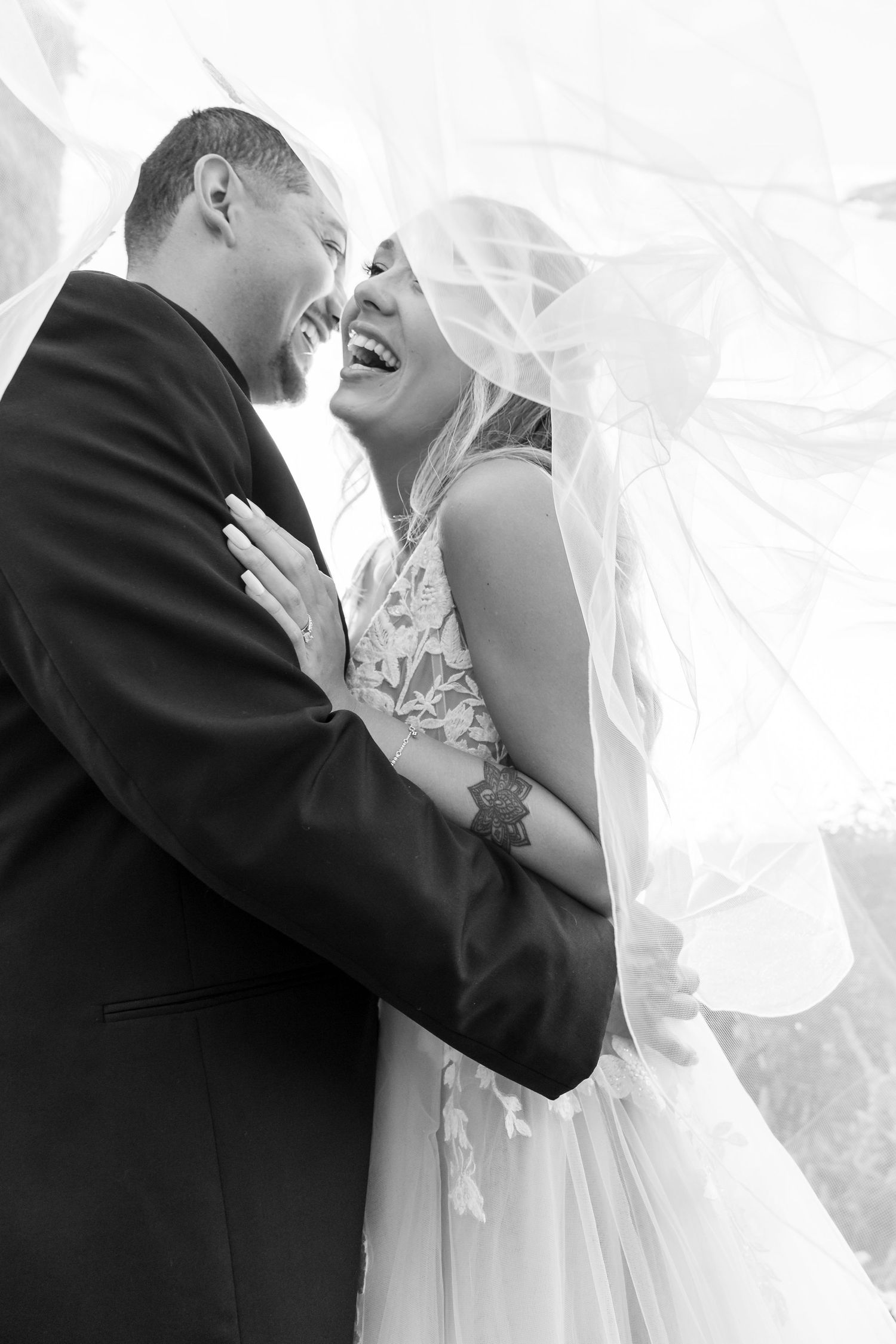 Intimate black and white portrait of newlyweds sharing a joyful moment under flowing veil.