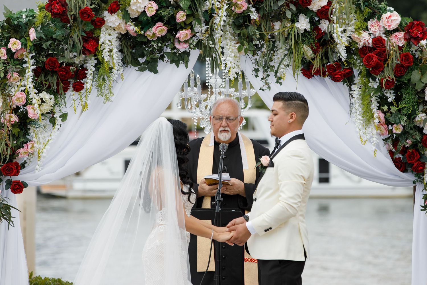 Wedding ceremony under floral arch with red and white roses and greenery decorations.