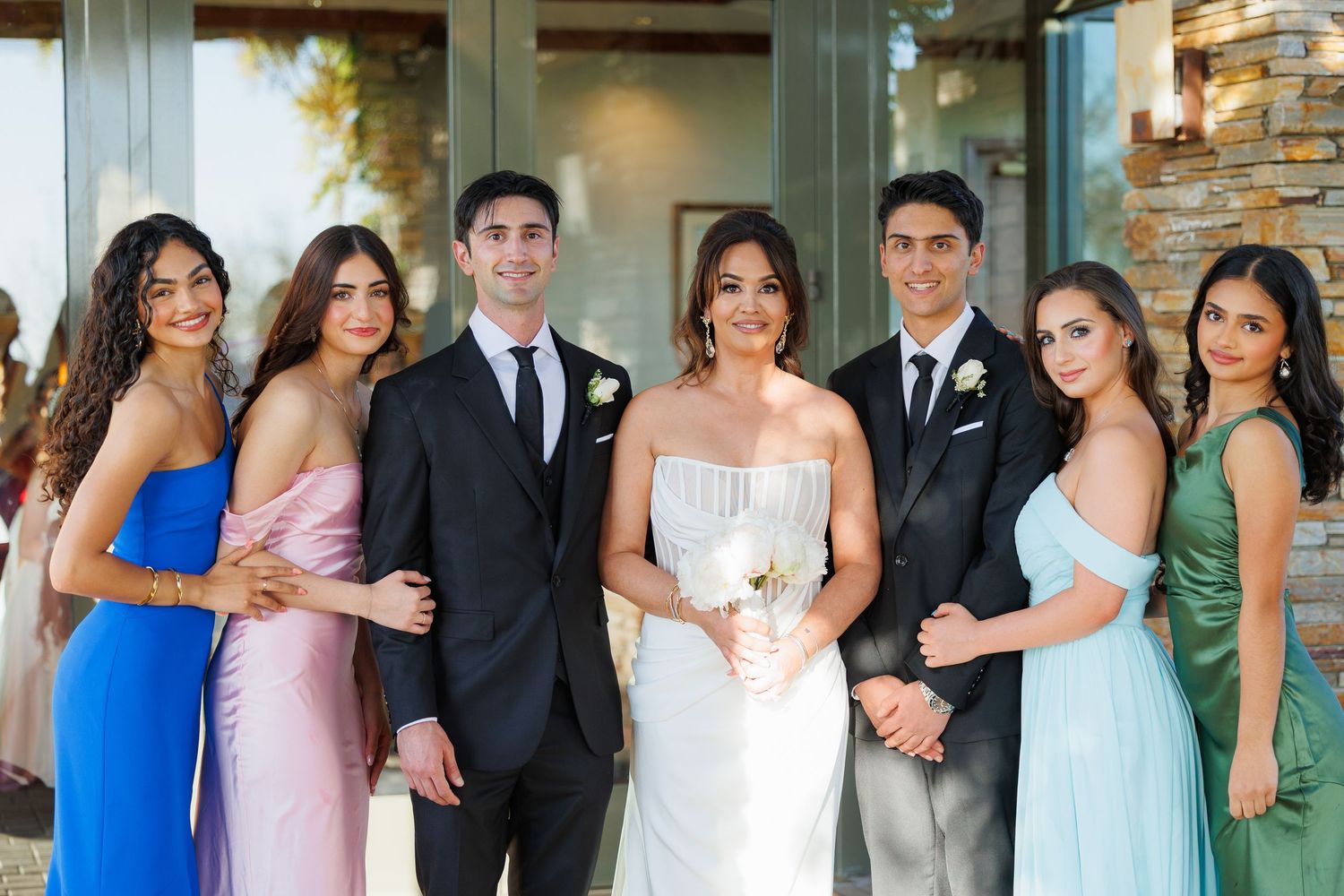 Wedding party members in pastel blue and pink dresses pose together in an elegant outdoor setting.