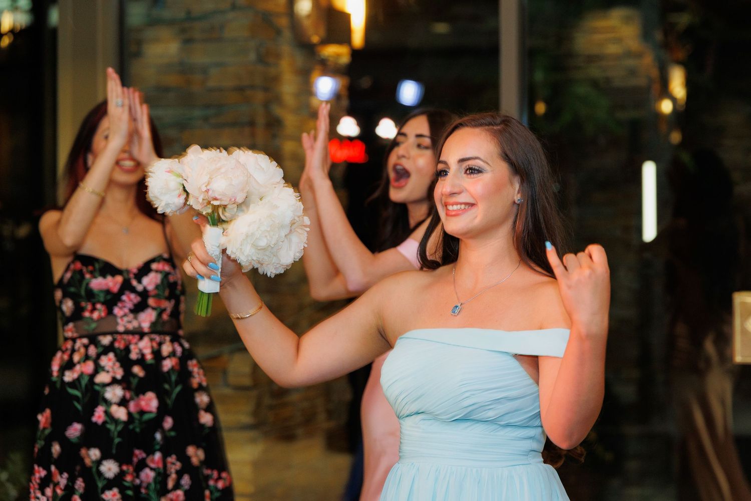 Wedding party dances together during reception celebration in dimly lit venue with warm lighting.