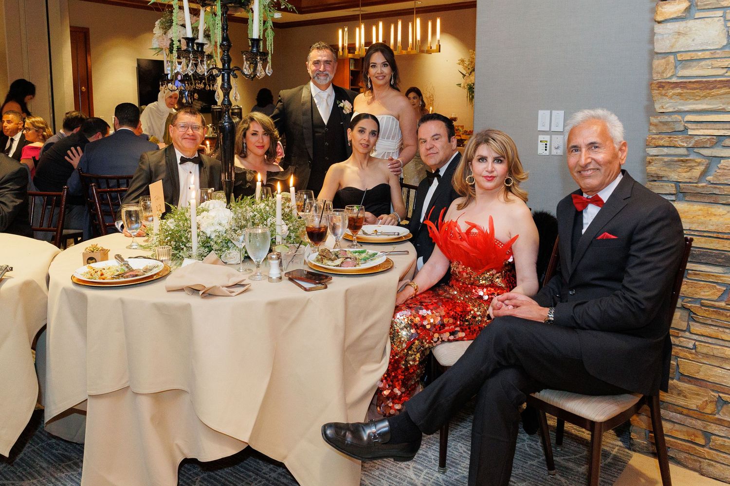 Wedding guests in formal attire seated at an elegant round dining table with candles and white tablecloth at reception.