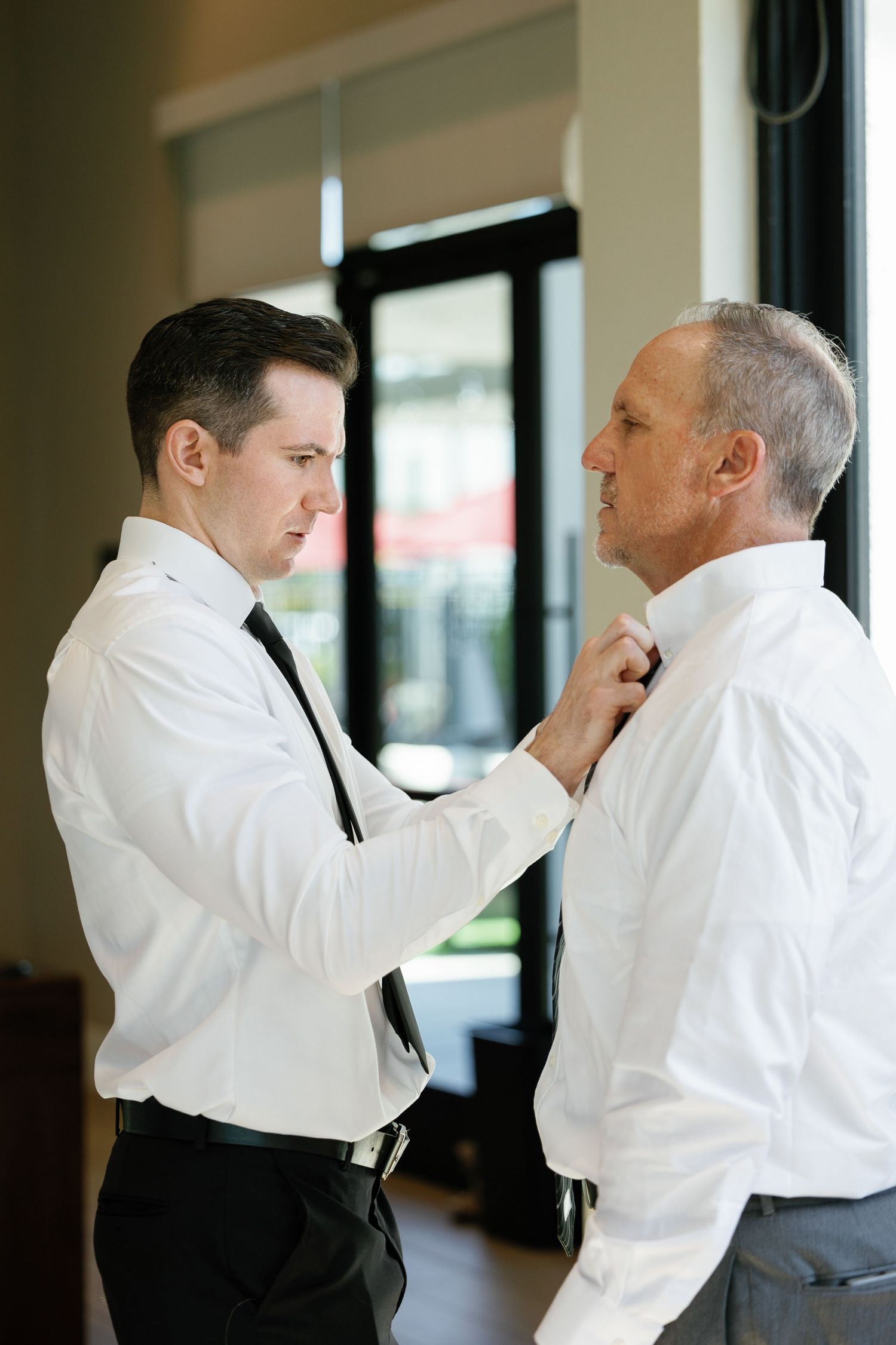 Two people in formal attire help adjust each other's bow ties and collars before an event.