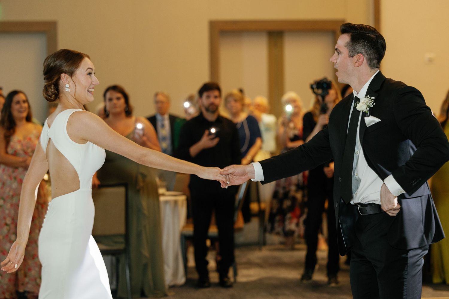 A couple shares their first dance at an elegant wedding reception while guests look on in the background.
