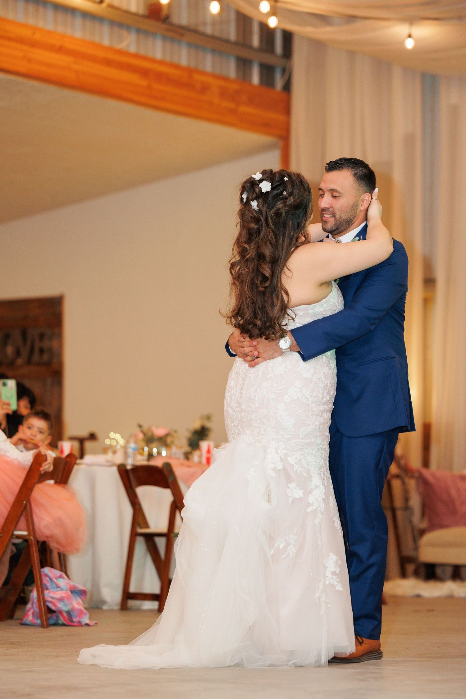 A romantic first dance sequence between newlyweds in white dress and navy suit at an elegant indoor reception venue.