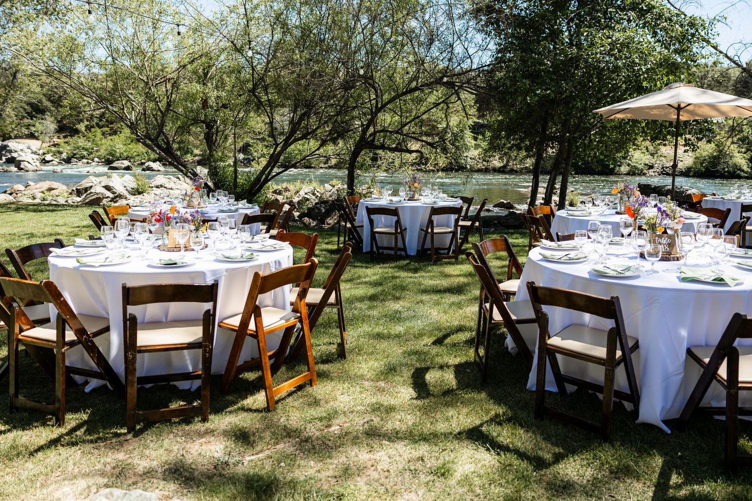 Round tables with white linens and wooden chairs set up outdoors for an elegant garden wedding reception.