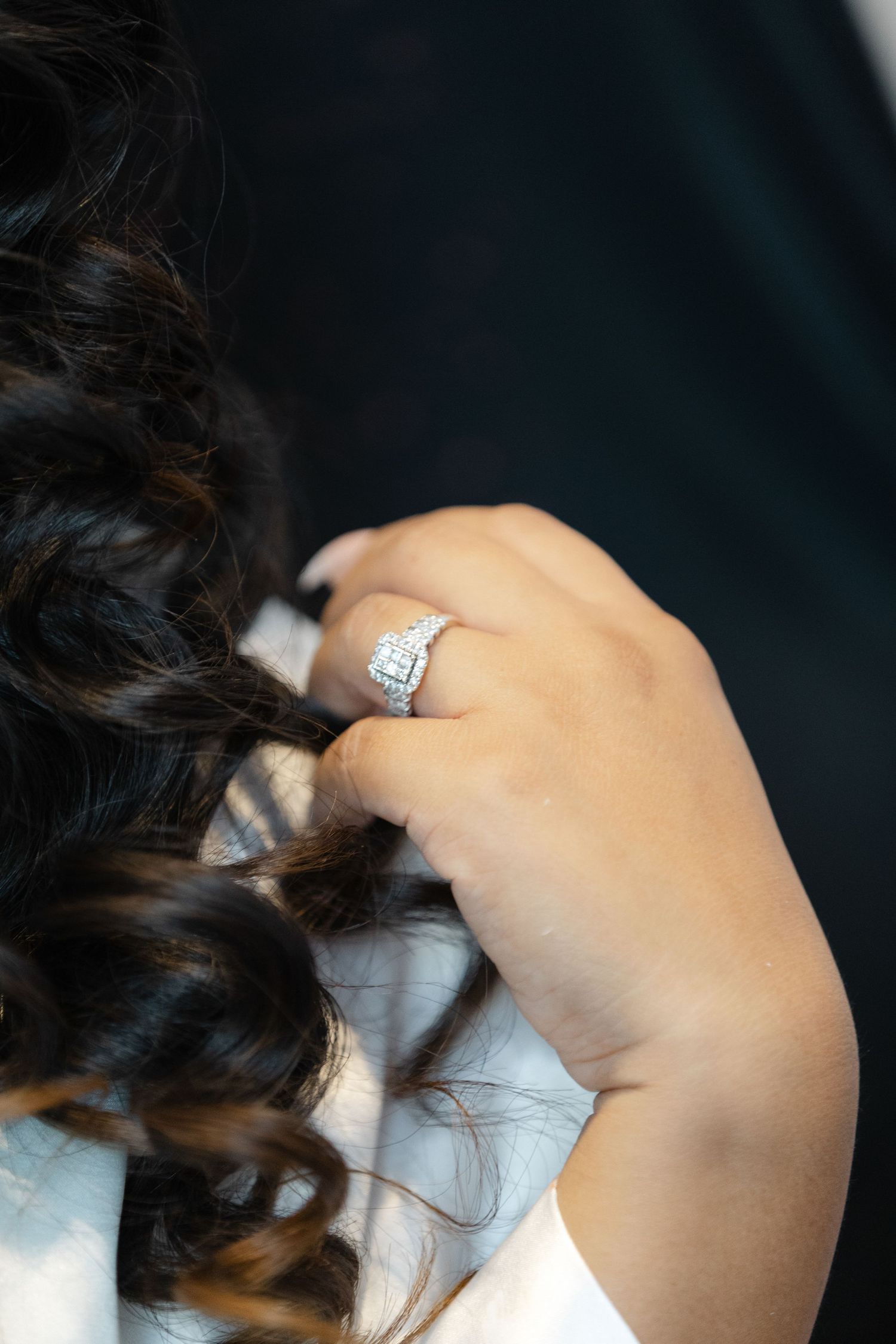 Close-up view of a sparkling diamond engagement ring on a hand against dark background.