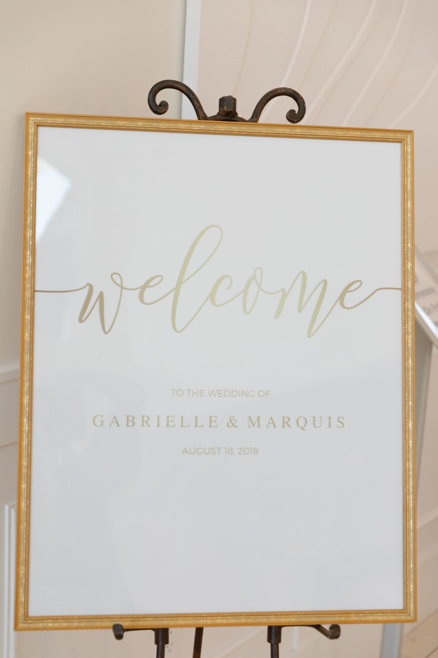 Elegant white and gold wedding welcome sign with calligraphy text displayed on a decorative metal easel.