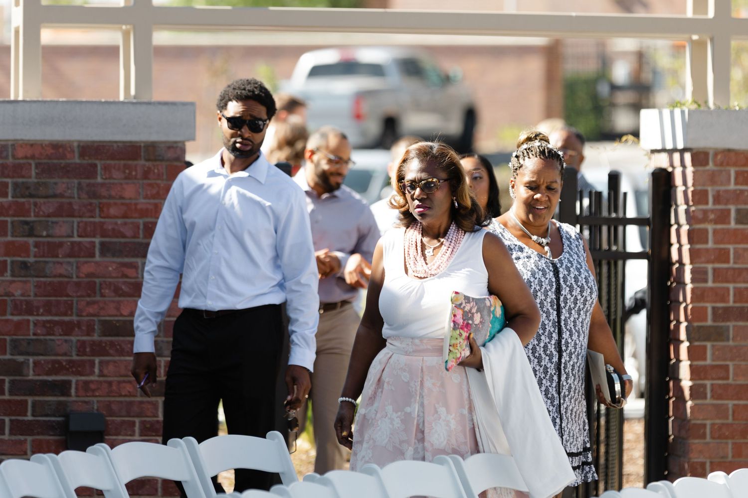 A group of people dressed in formal attire walk together through a brick entrance during a special occasion.