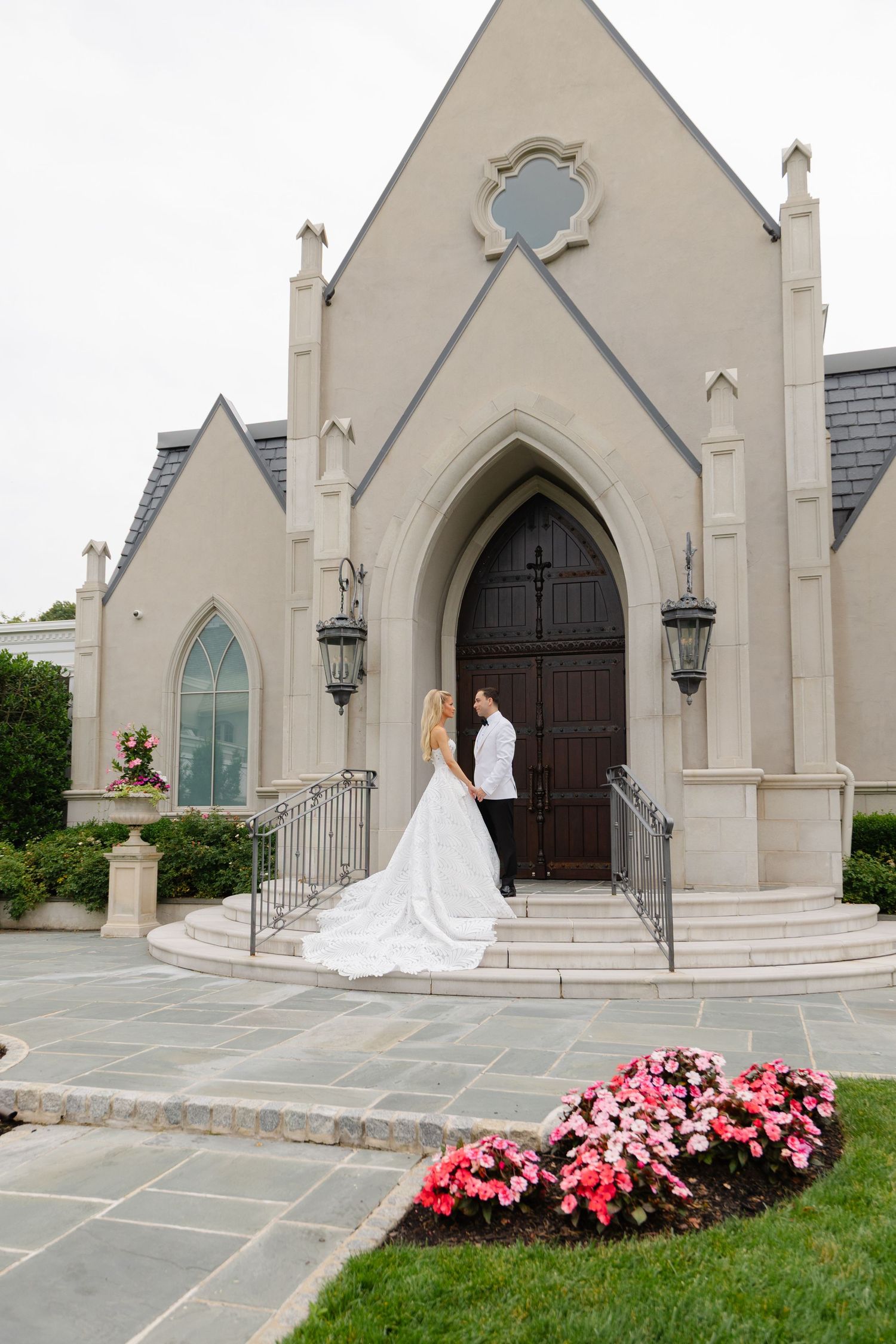 A couple stands on stone steps outside a Gothic-style church with cream colored walls and arched doorways.
