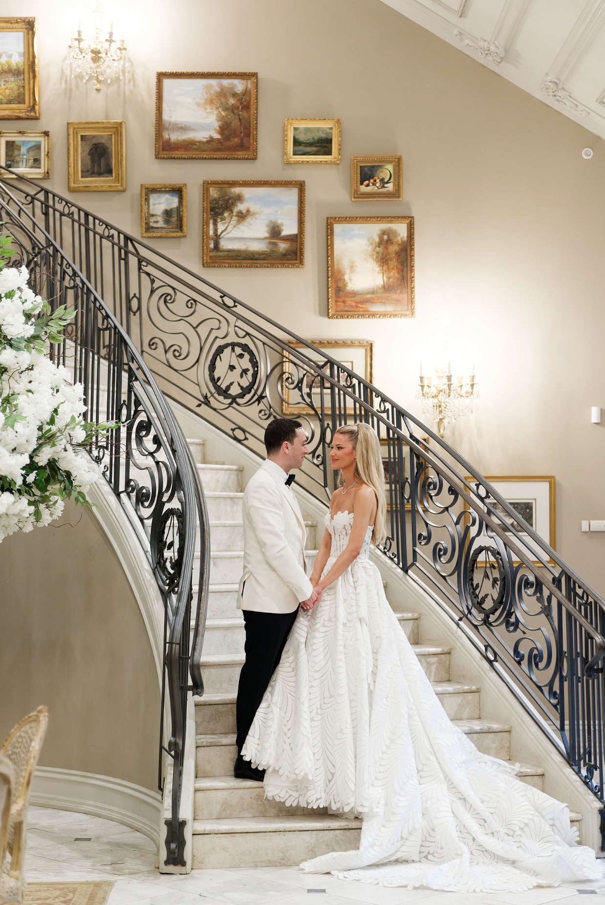 A series of elegant wedding photos showing the train of a white lace gown flowing down an ornate staircase with framed art.