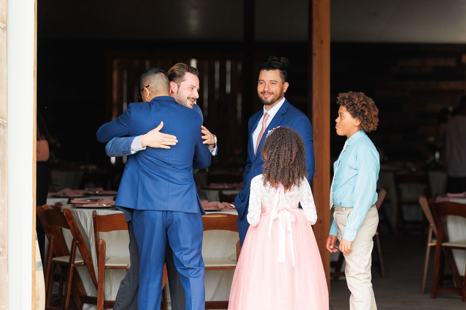 People gathered in a dimly lit indoor venue sharing hugs and greetings at what appears to be a social event.