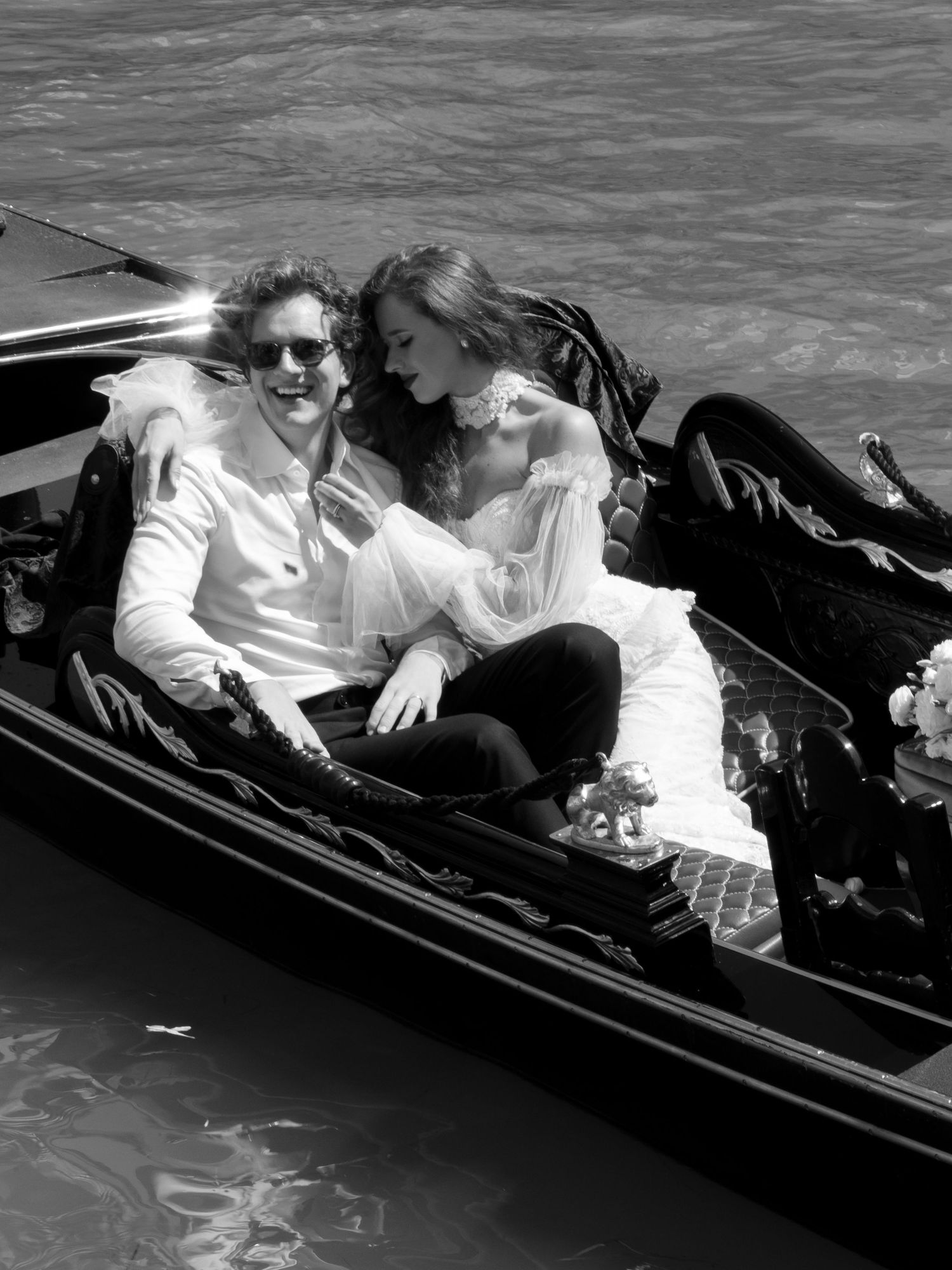 A romantic black and white photo of a couple lounging together in a gondola on the water.