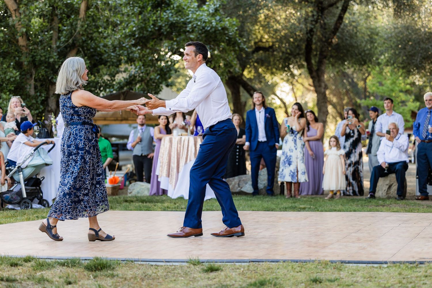People dancing together outdoors at a summer wedding reception in a park setting with natural lighting.