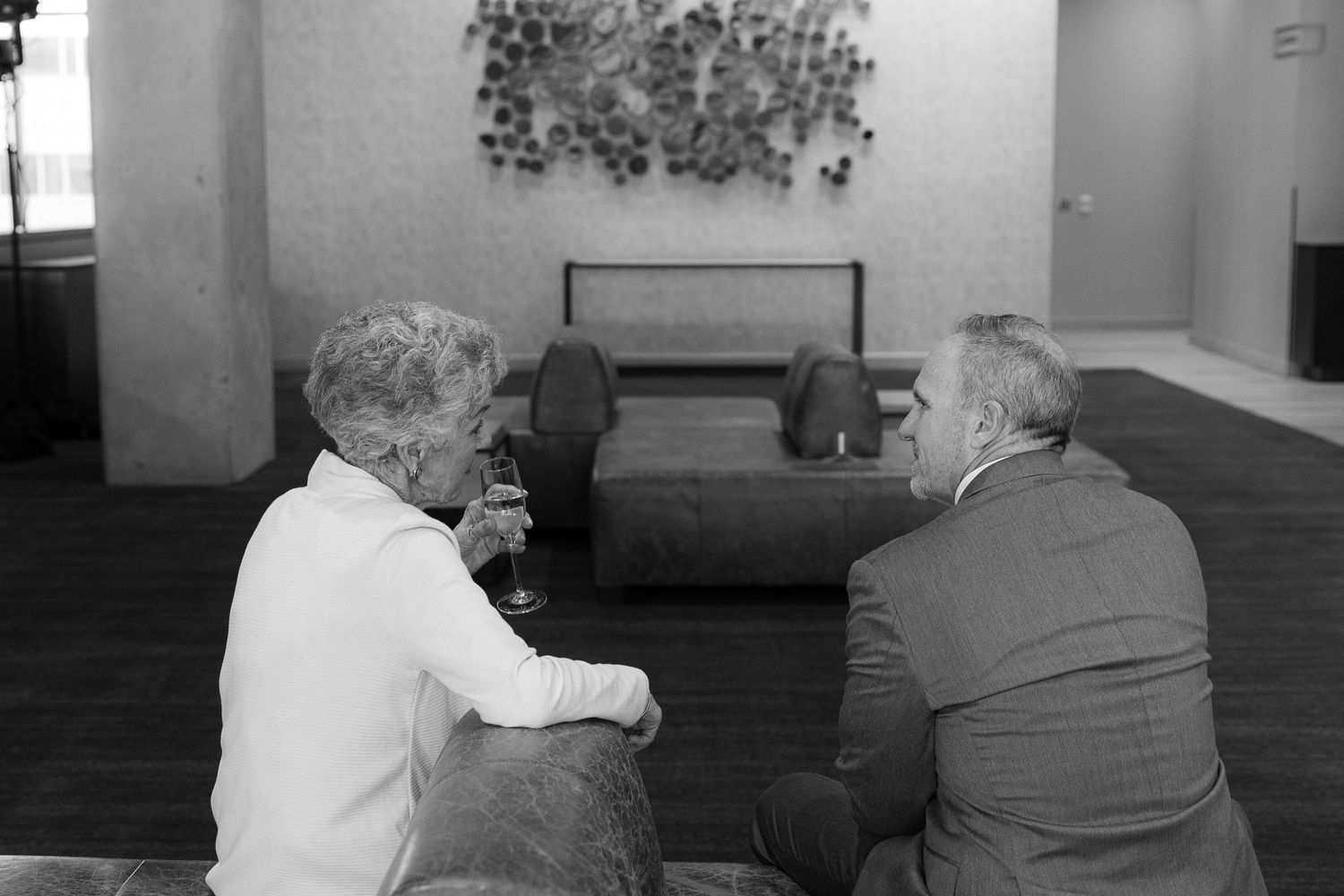 Two people sit together in conversation at a table in what appears to be a restaurant or cafe setting.