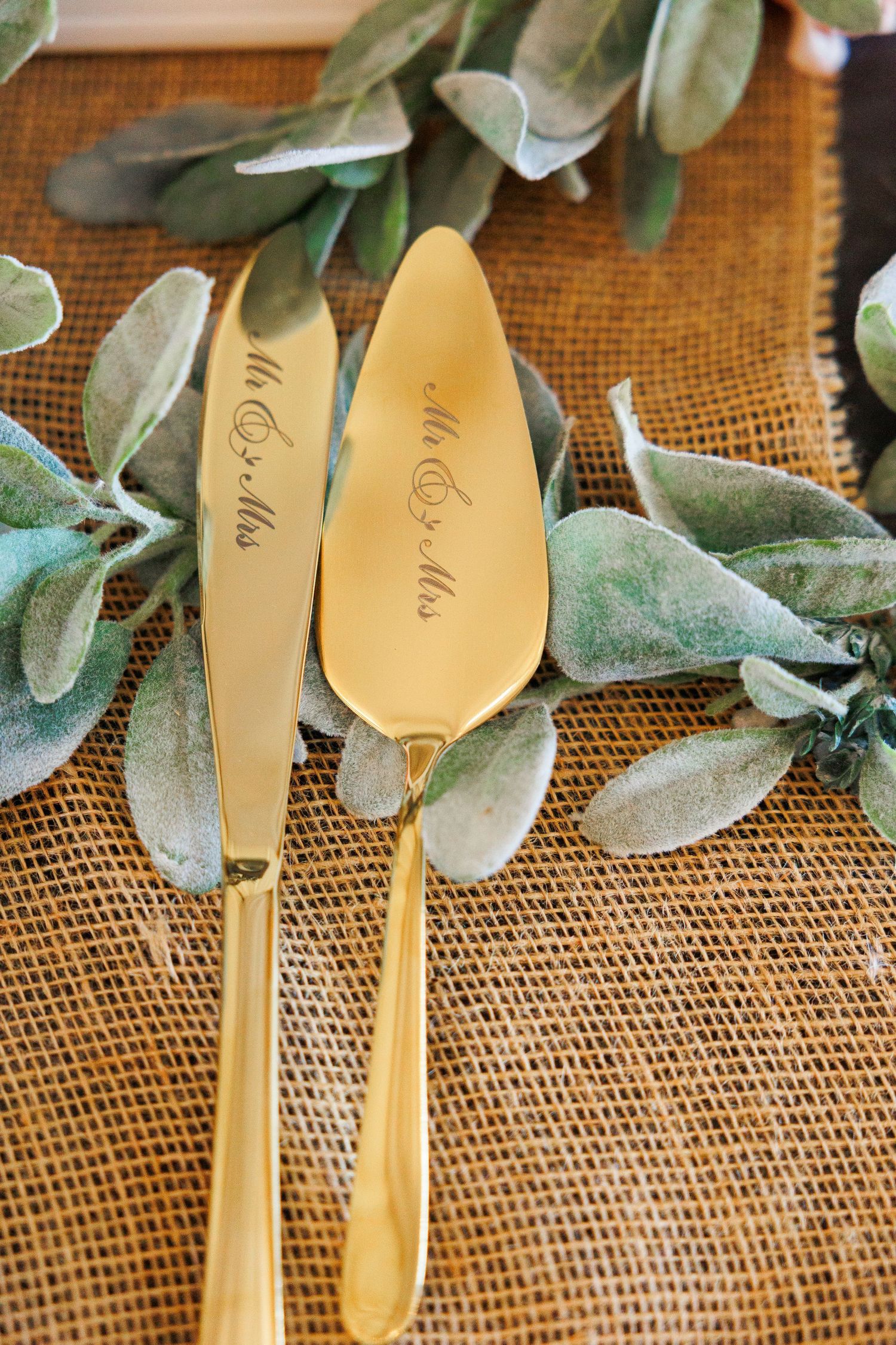 Personalized wooden spoons with engraved names arranged on burlap fabric with eucalyptus leaves as decoration.