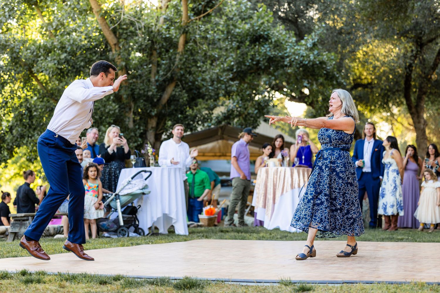 People dancing together in a park during a social outdoor event with trees in the background.